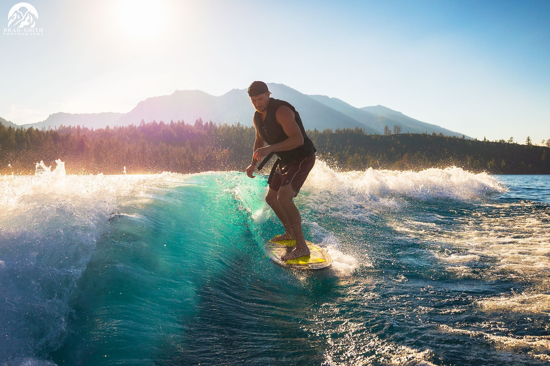 Surfer riding a turquoise wave at sunset with mountains in the background