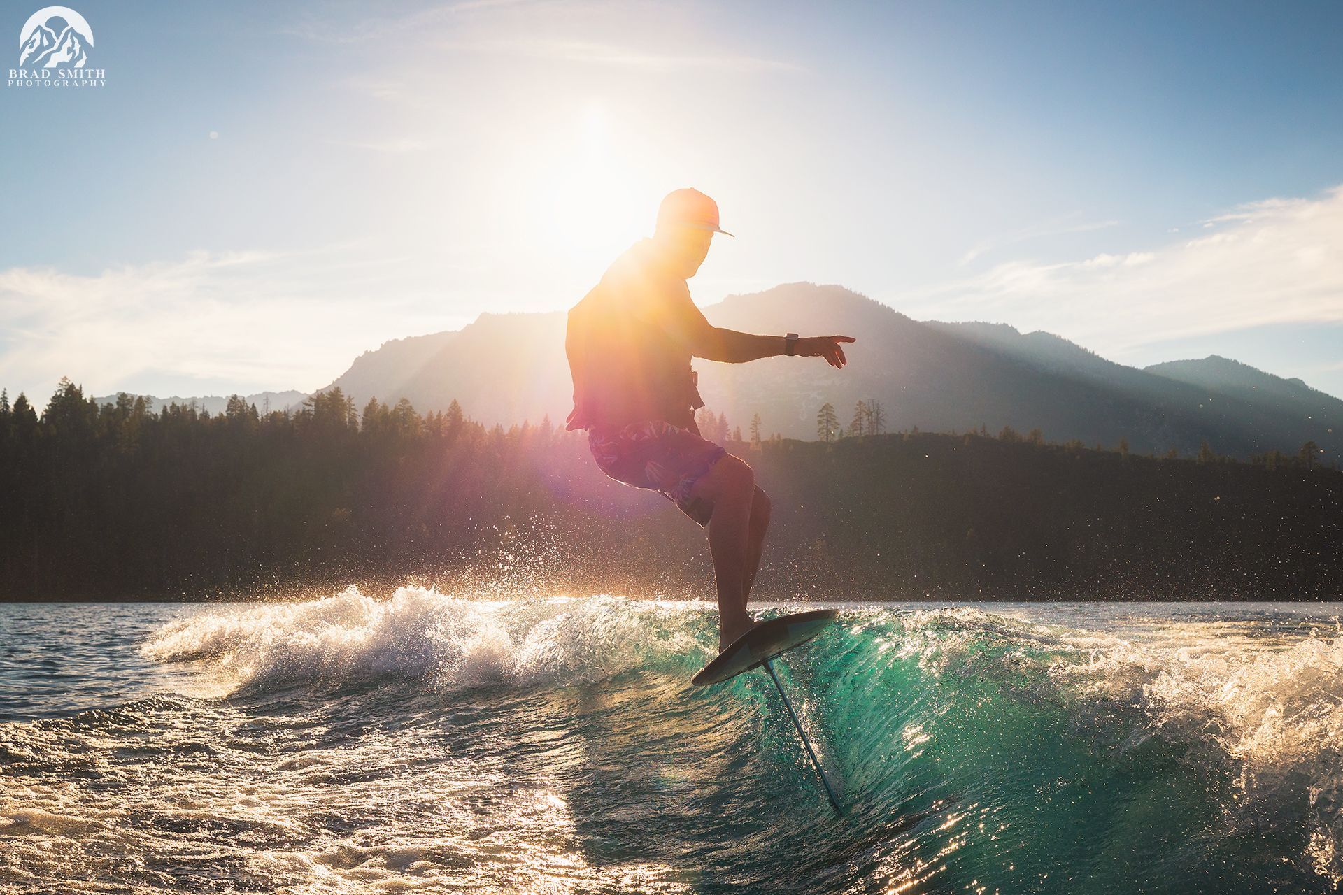 Silhouette of a person wakeboarding on a sunlit lake with mountains in the background