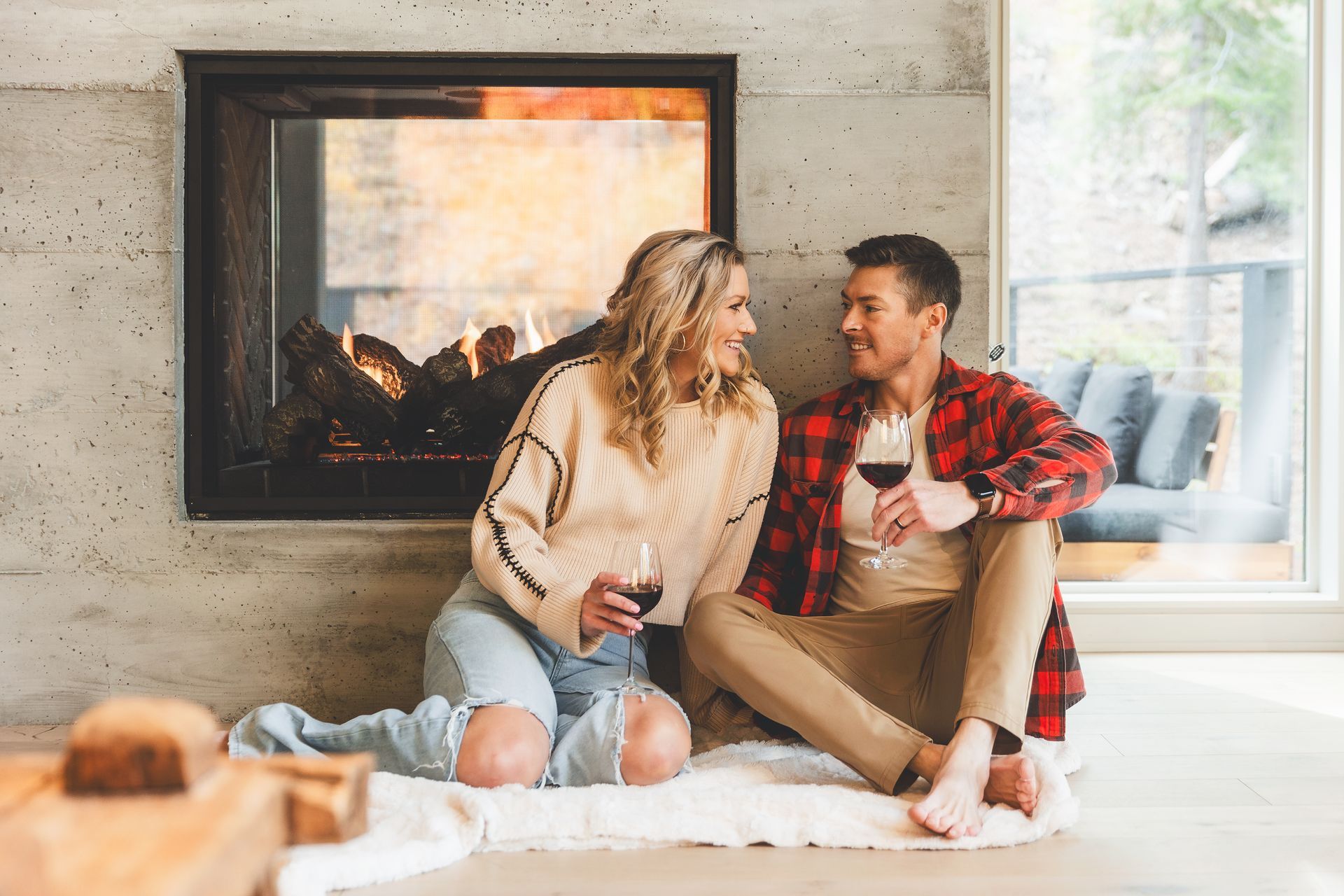 Two people sitting on a rug by a fireplace, smiling and talking in a bright living room