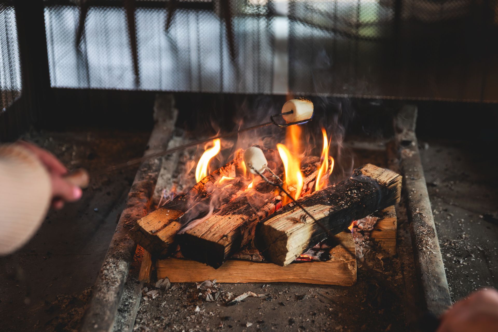 Fire burning in a fireplace with stacked logs and a hand tending the flames