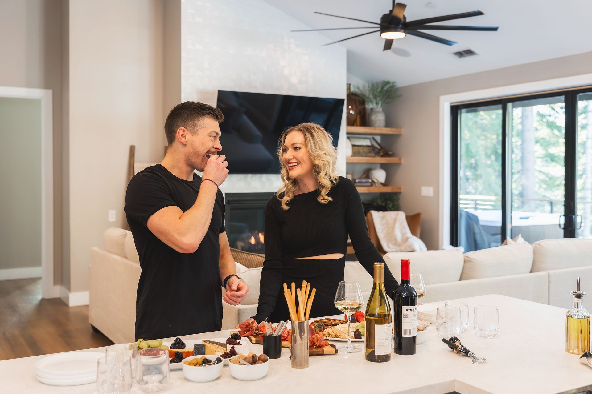 Two people chatting in a bright kitchen with snacks and wine on the counter