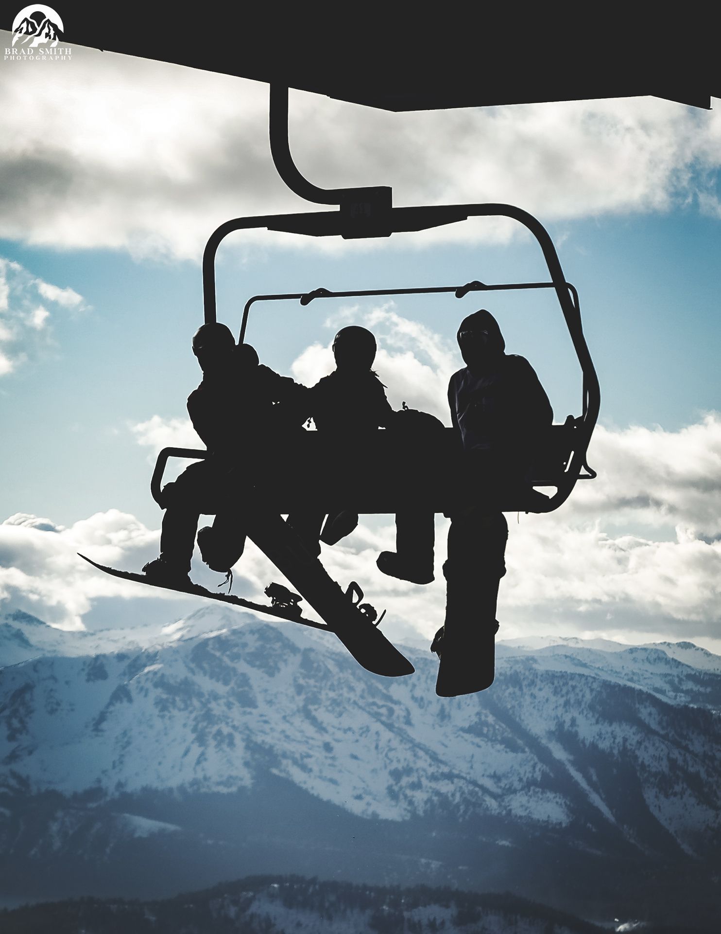 Silhouetted skiers on a chairlift above snowy mountain slopes under a cloudy sky
