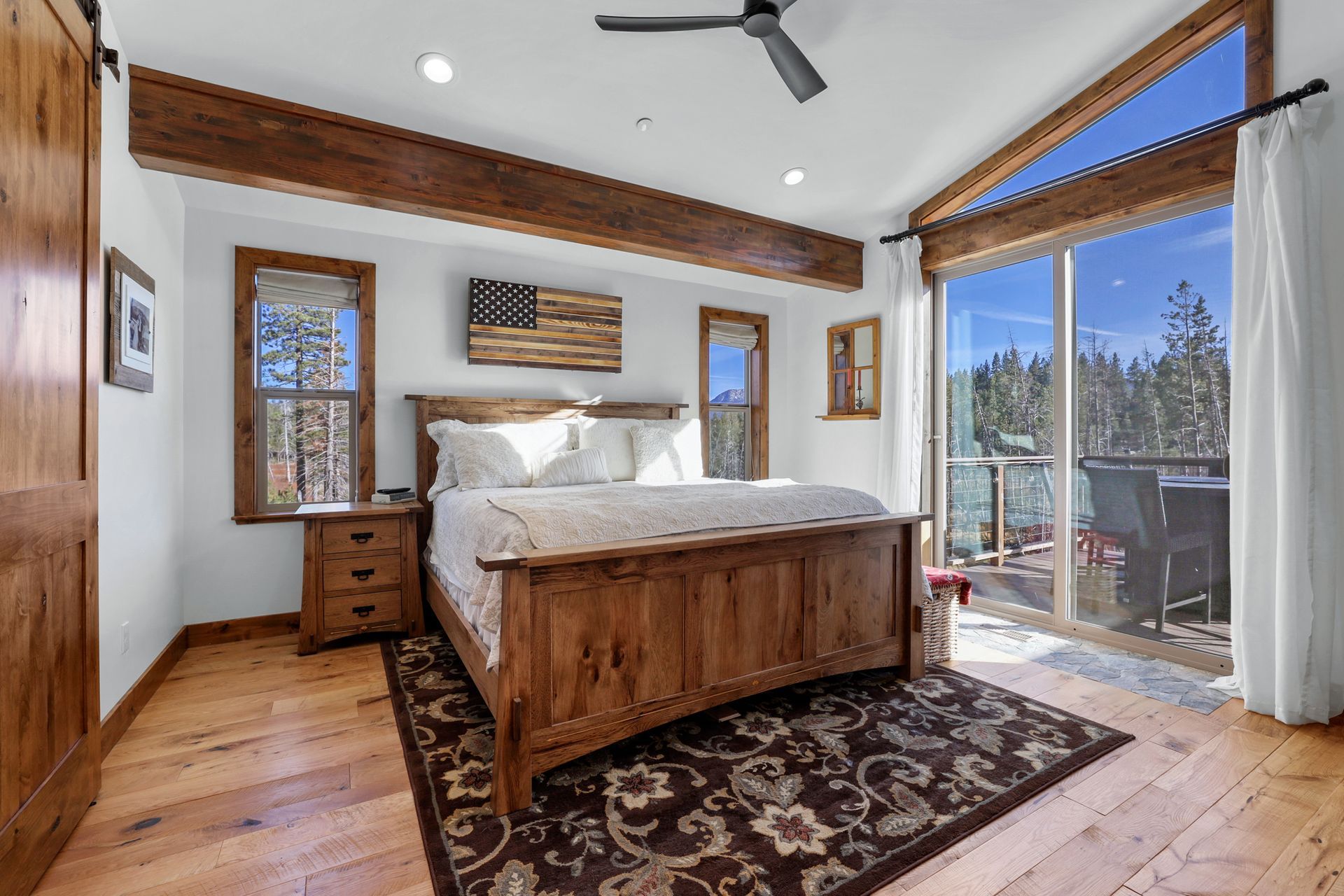 Spacious rustic bedroom with a wooden bed, patterned rug, and large sliding glass doors to a balcony.