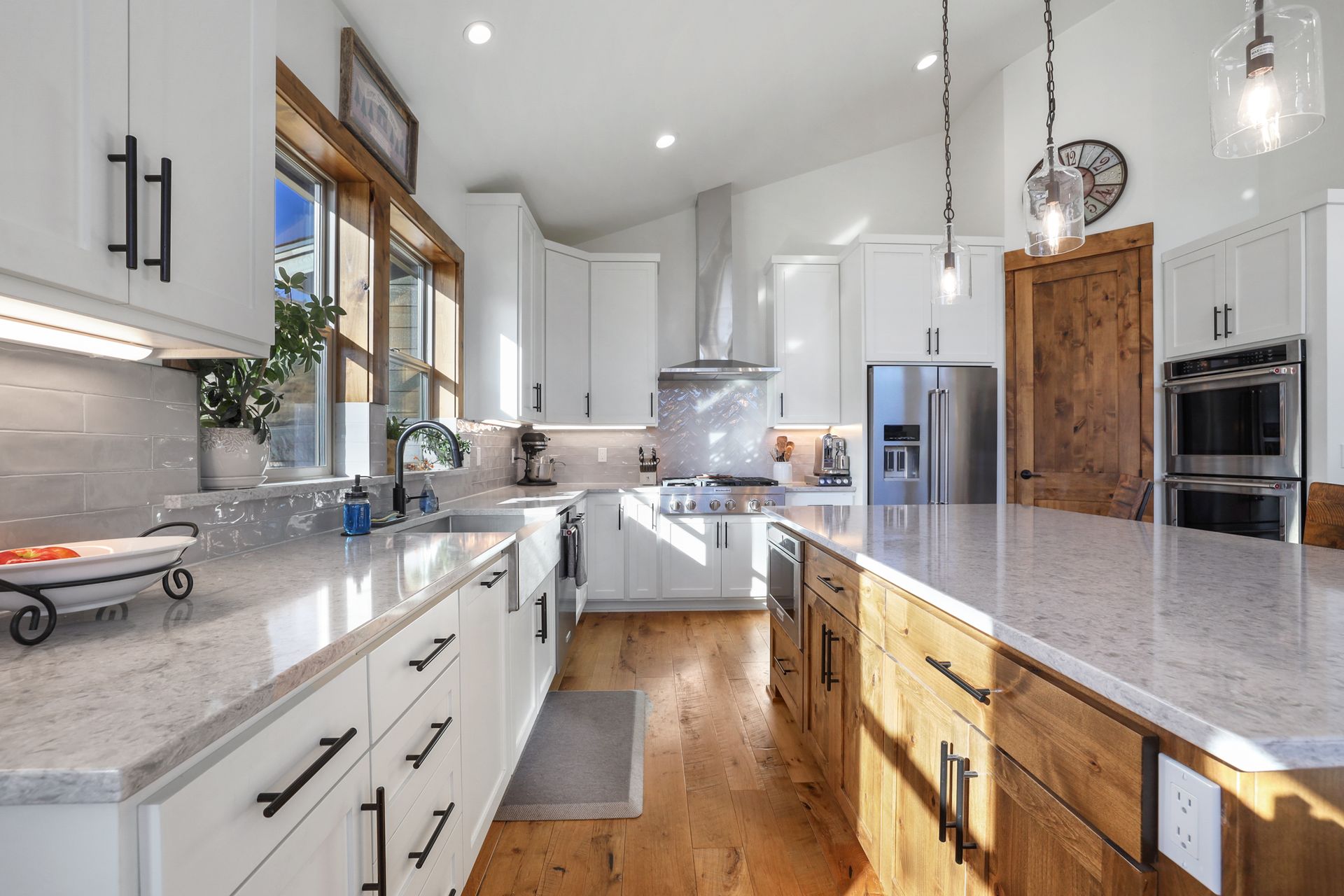 Bright modern kitchen with white cabinets, marble counters, stainless appliances, and wood floors