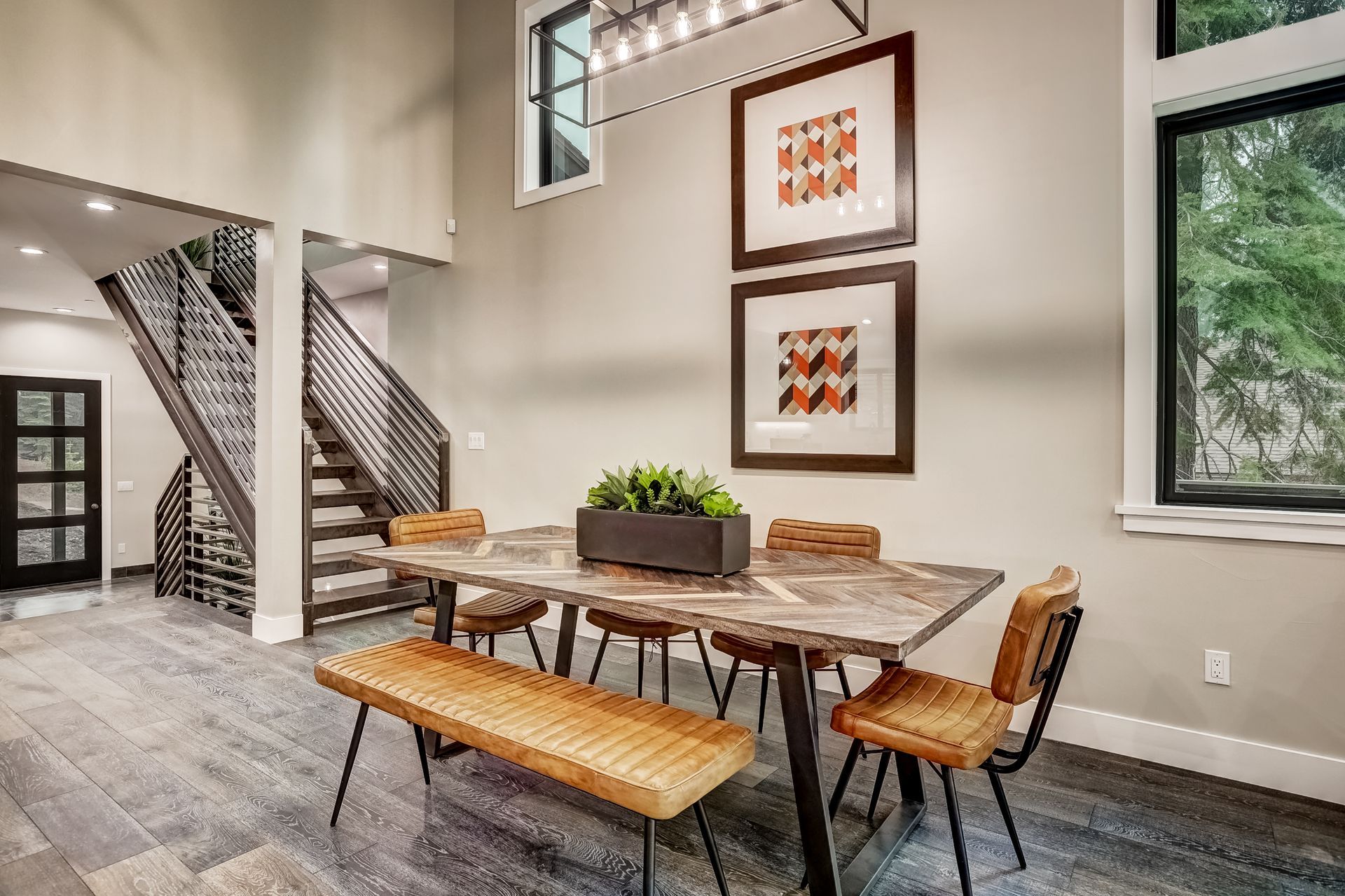 Bright dining room with rustic table, bench seating, wall art, stairs, and large windows