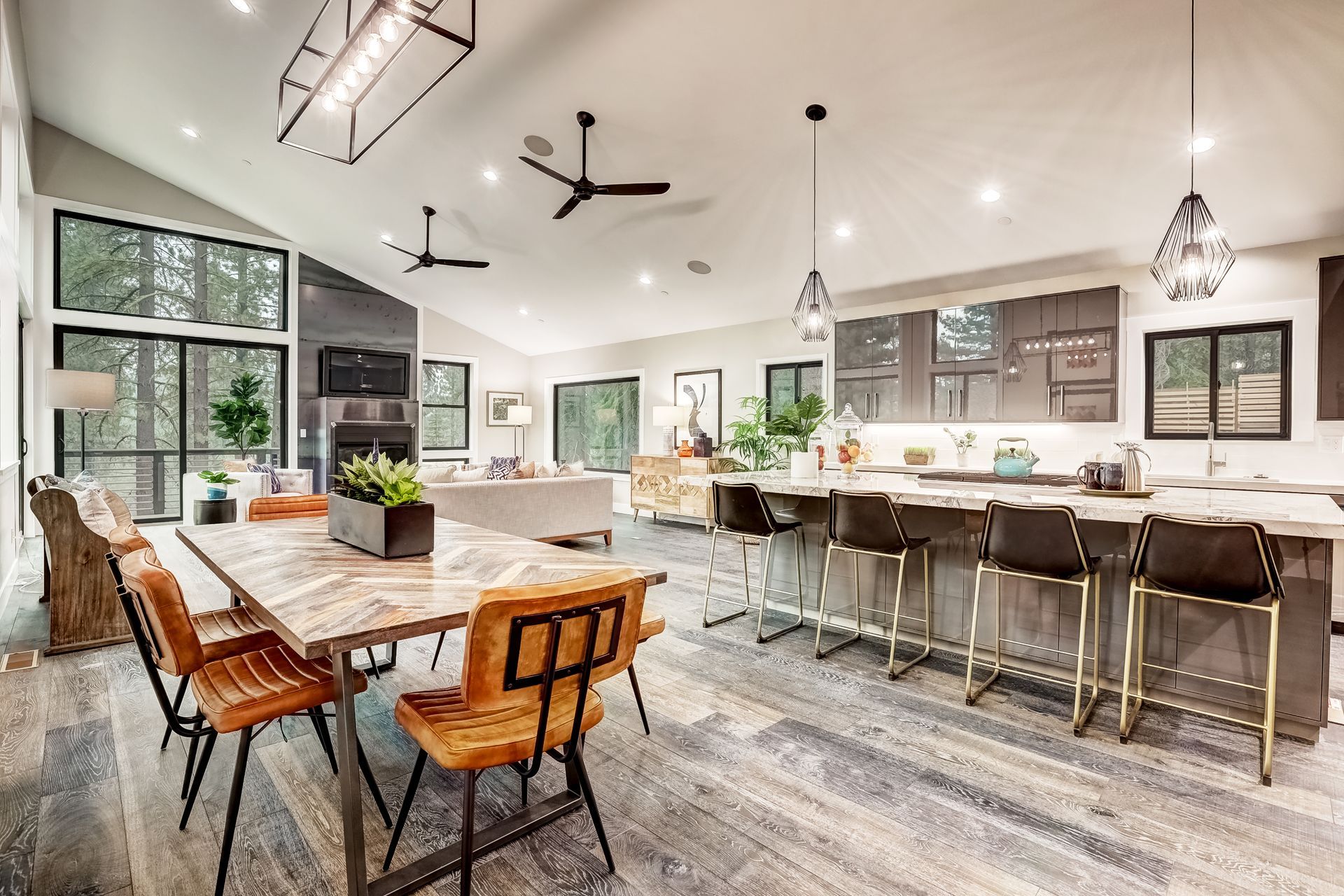 Bright modern kitchen-dining space with long wooden table, island seating, and large windows
