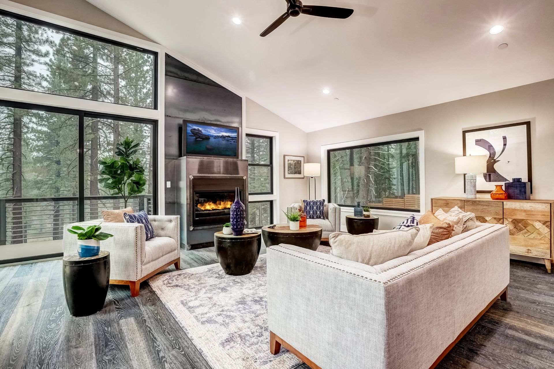 Bright modern living room with large windows, fireplace, sectional sofa, and mountain forest view