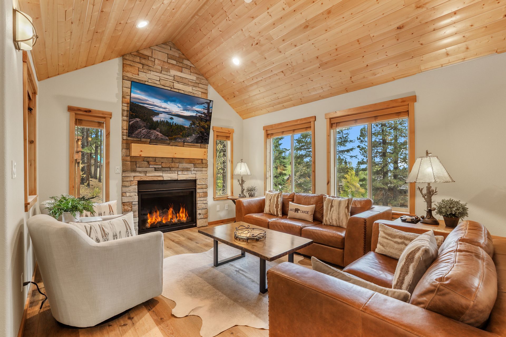 Cozy living room with wood vaulted ceiling, fireplace, leather sofa, and large windows overlooking trees