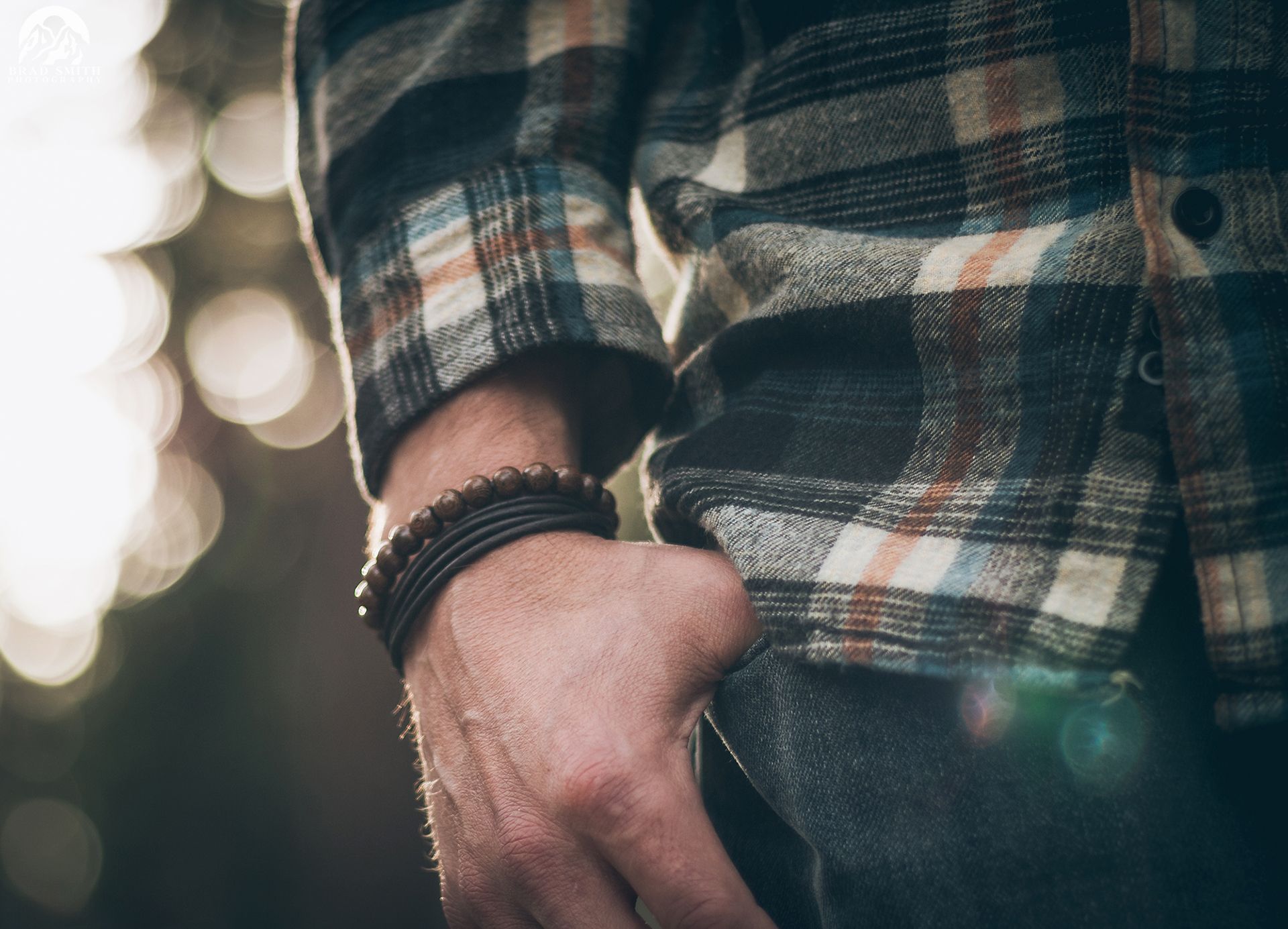 Close-up of a hand in a plaid shirt, wearing stacked black bracelets, against a blurred background