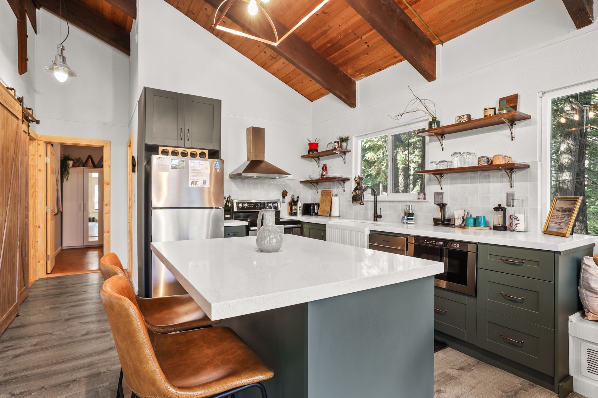 Modern kitchen with white island, green cabinets, wood beam ceiling, and pendant lights