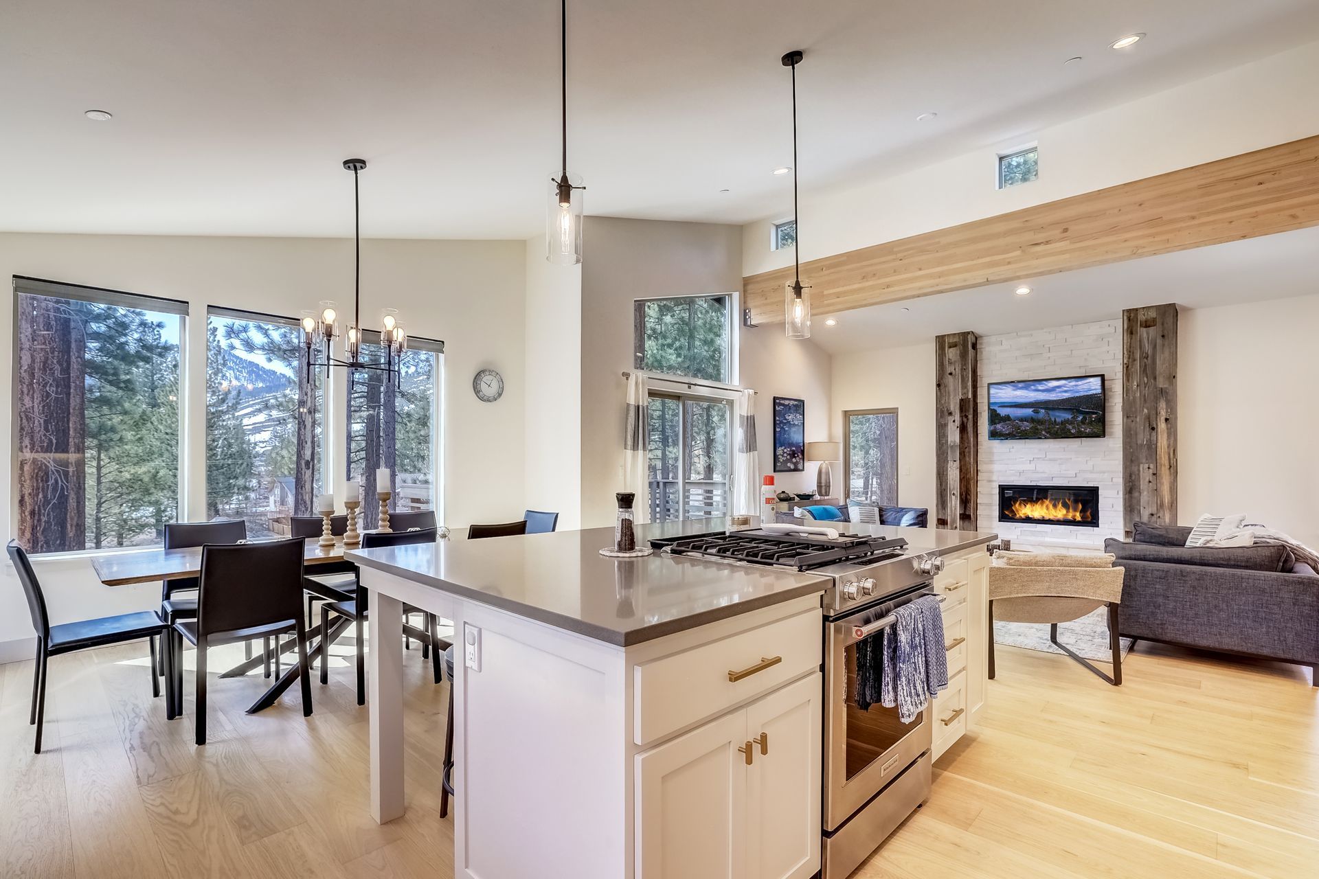 Bright open kitchen and living room with island, dining table, fireplace, and large windows