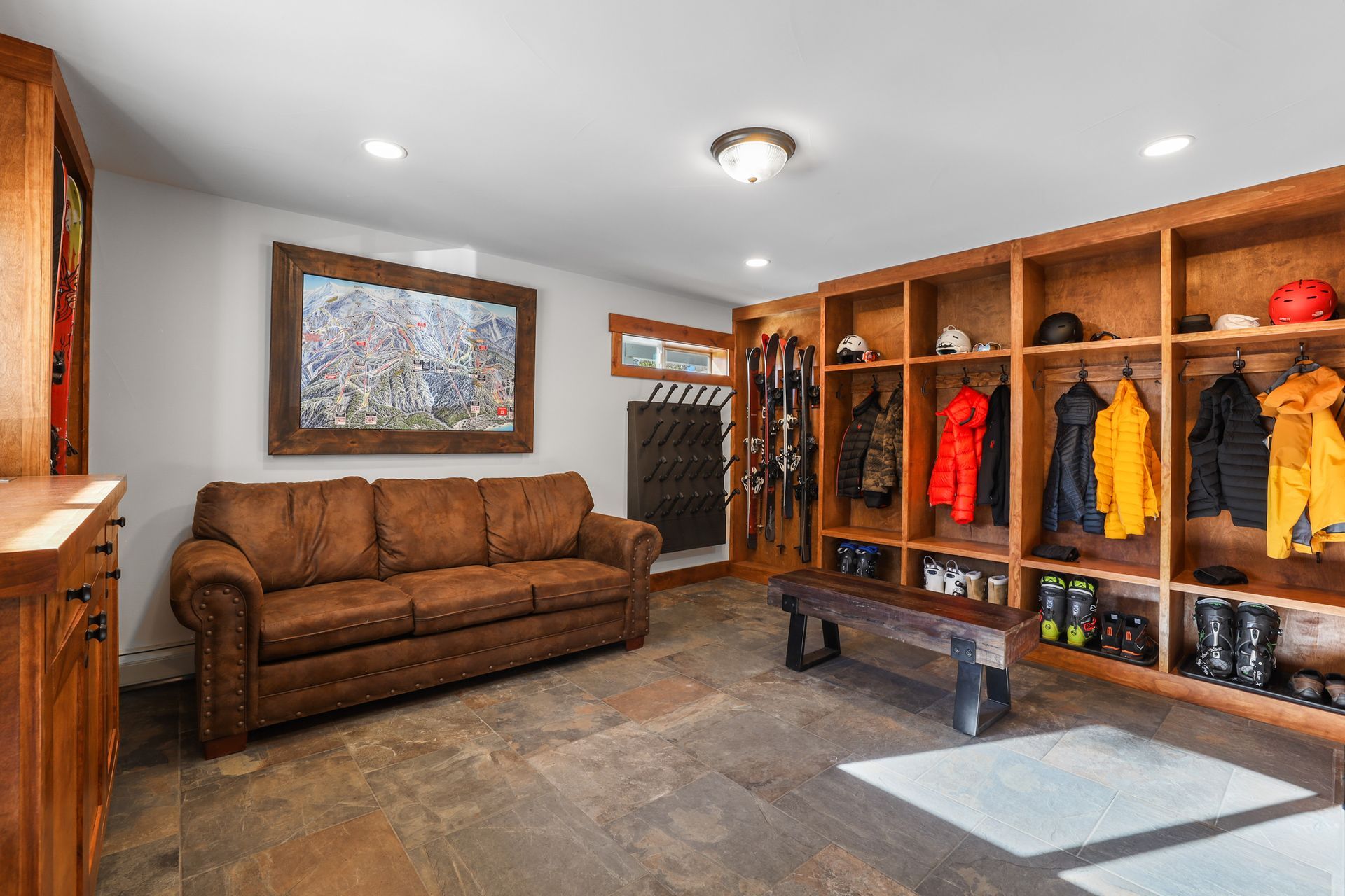 Mudroom with brown couch, wooden cubbies, coats, and boots on a tiled floor