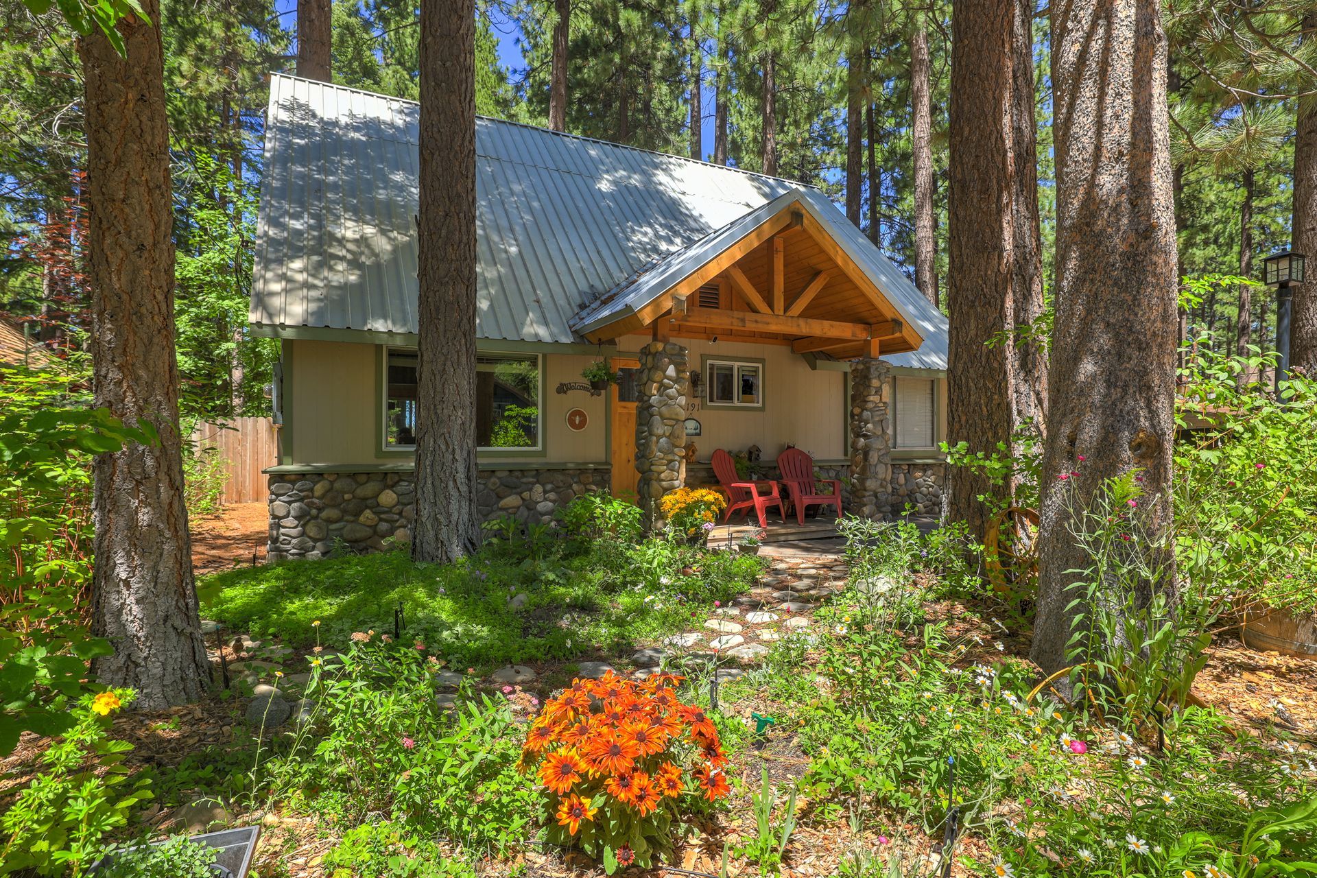 Cabin with a metal roof nestled among tall pine trees, with orange flowers in the foreground.