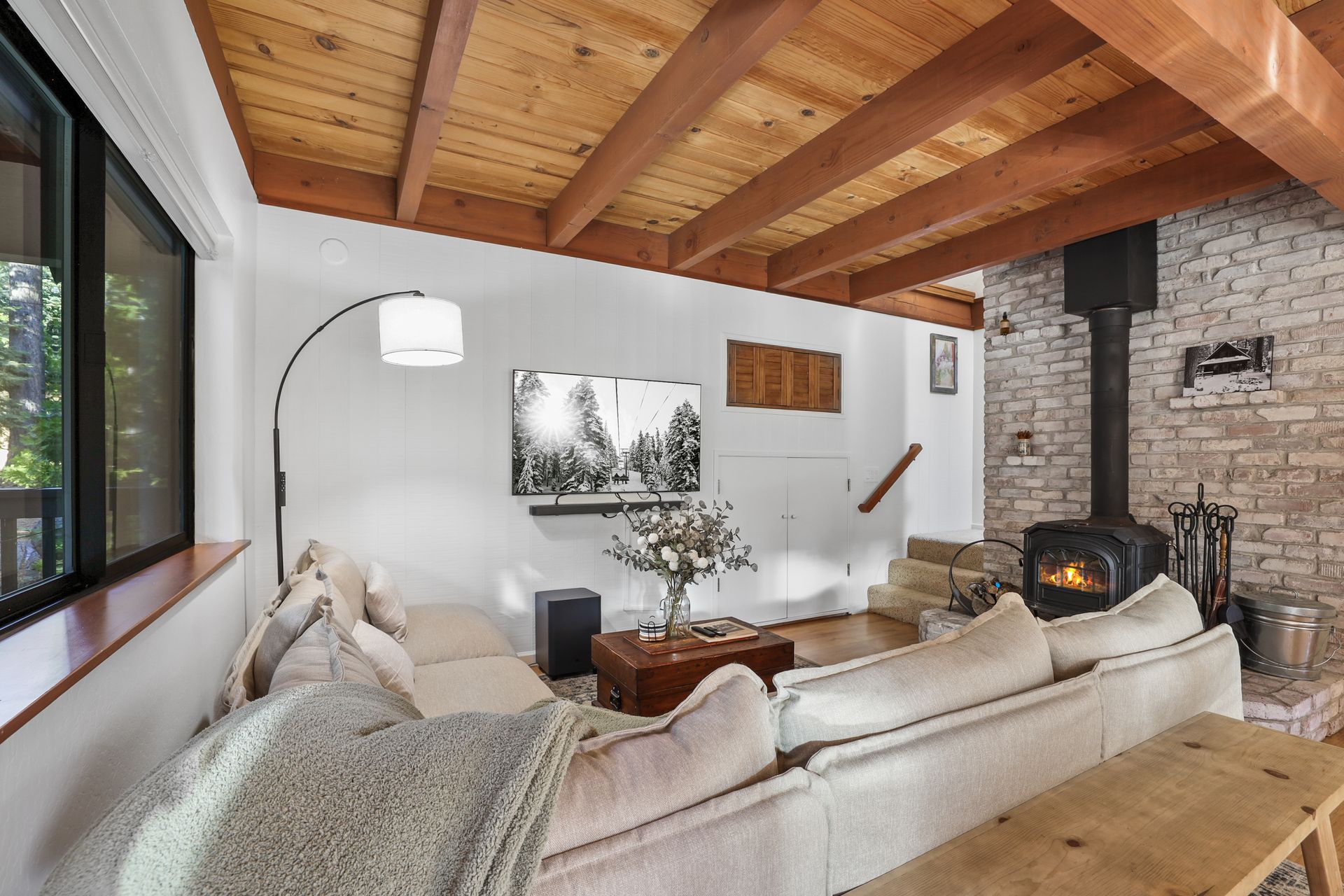 Cozy living room with beige sofa, wood-beamed ceiling, stone fireplace, and large window view
