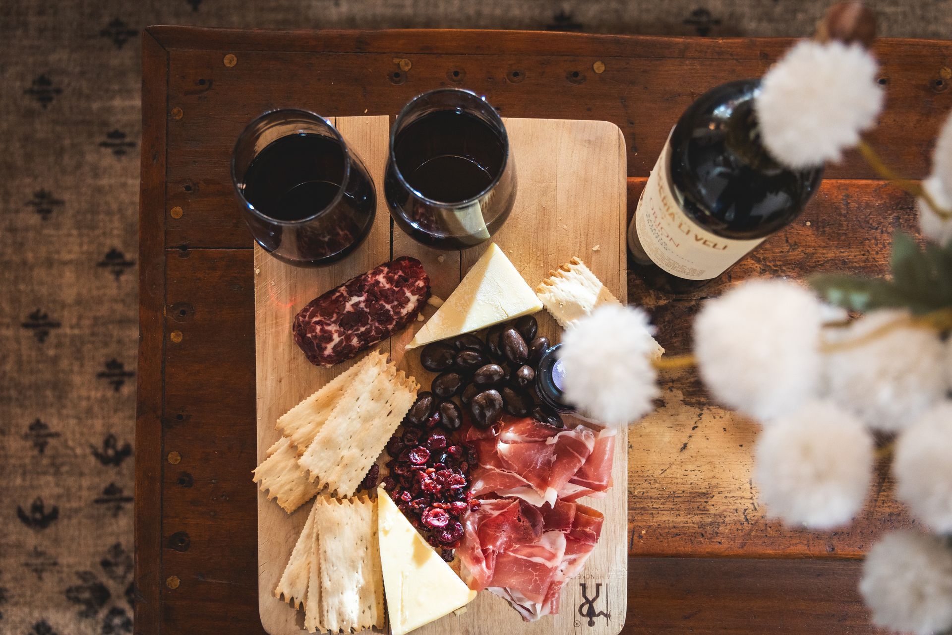 Charcuterie board with sliced meats, cheese, crackers, and two glasses of red wine on a wooden table