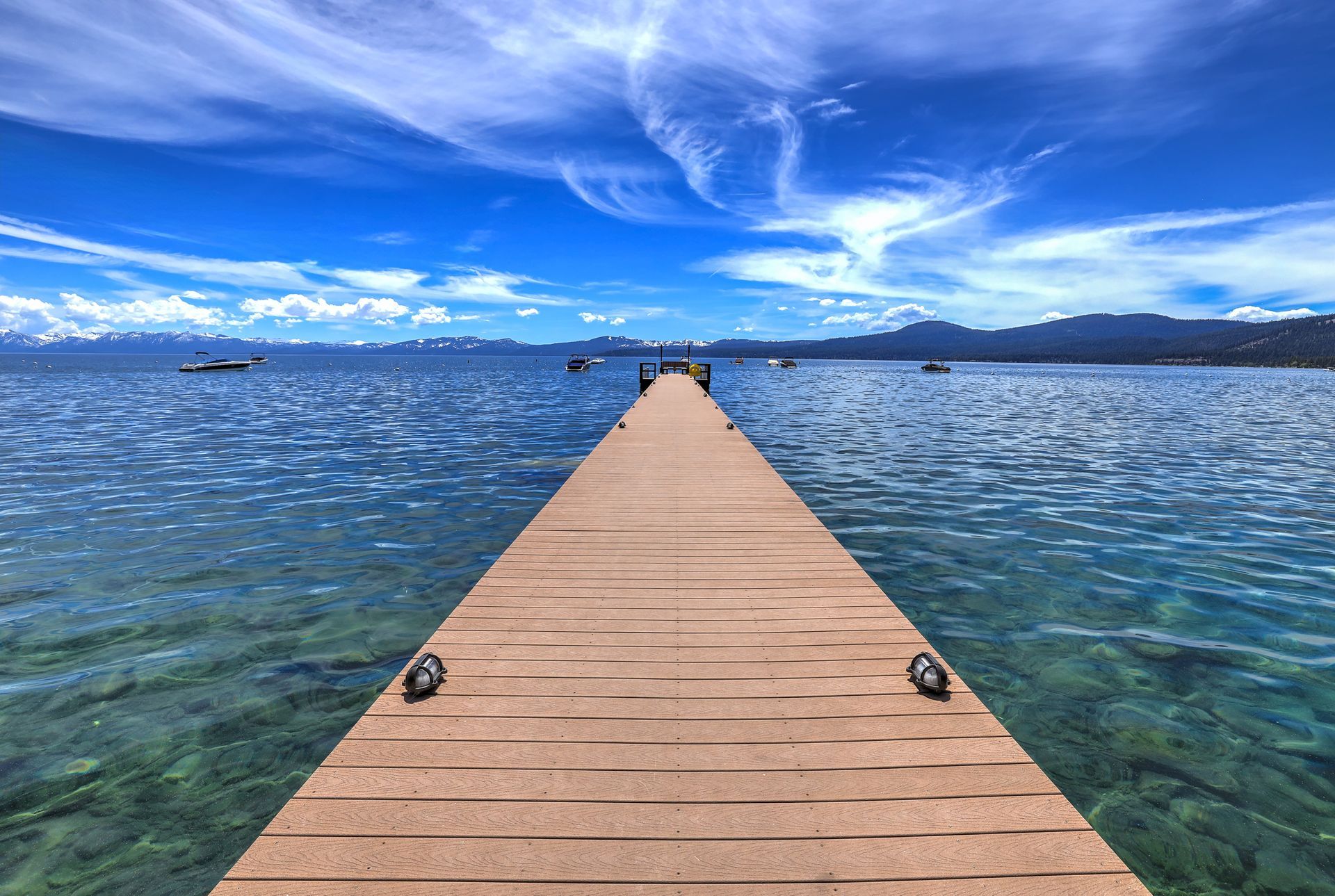 Wooden pier stretching into a blue lake under a bright sky with wispy clouds