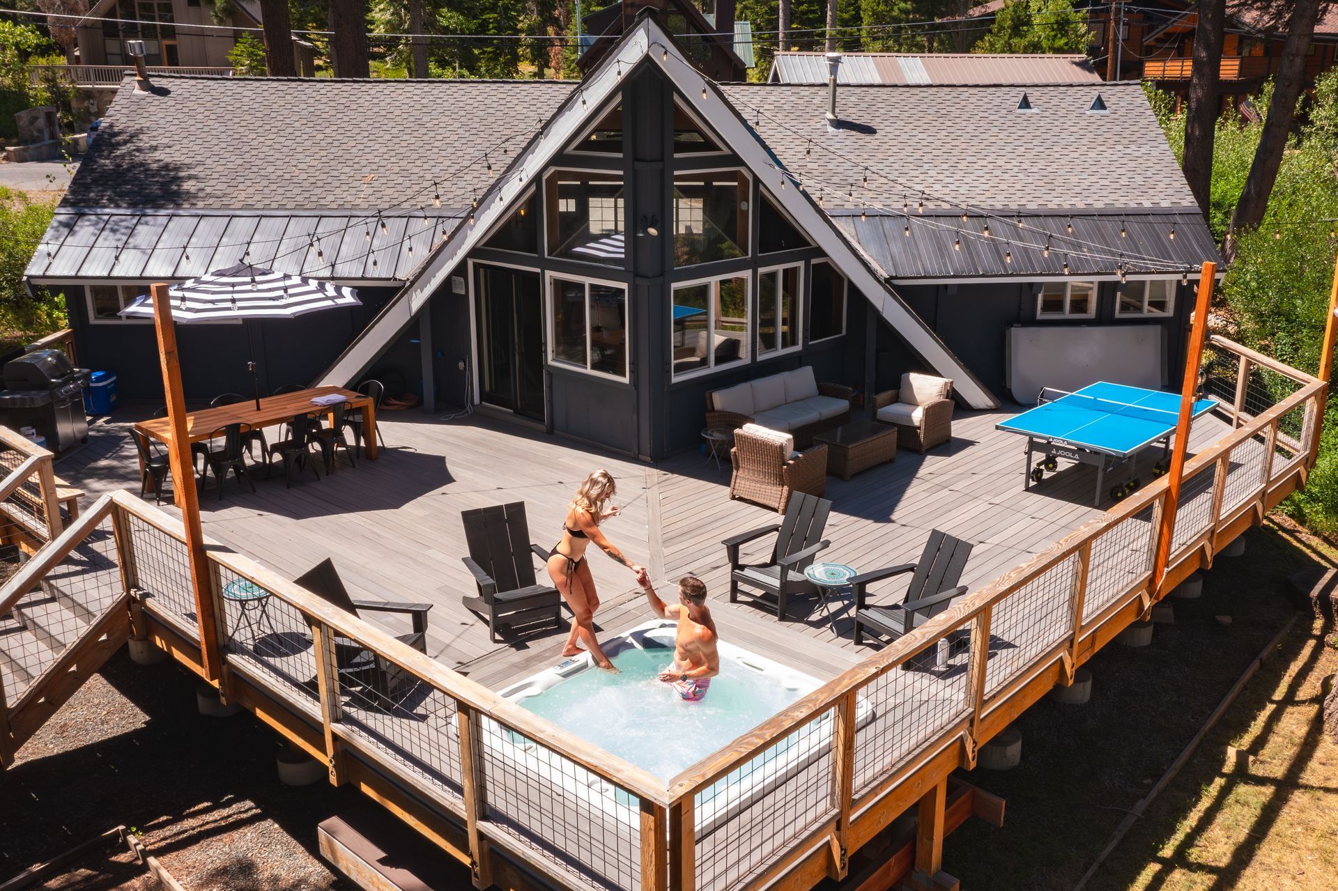 Wooden deck with a small pool and lounge chairs beside a modern cabin in the woods