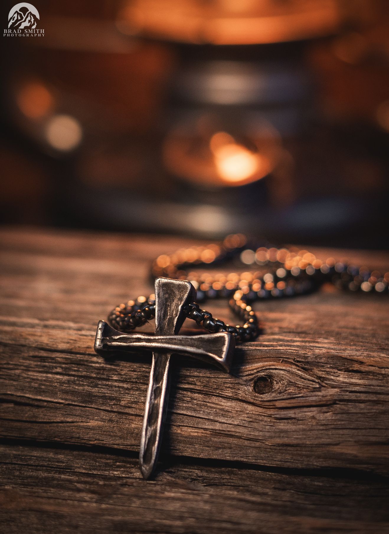 Cross pendant necklace on a wooden table with a warm blurred candlelit background