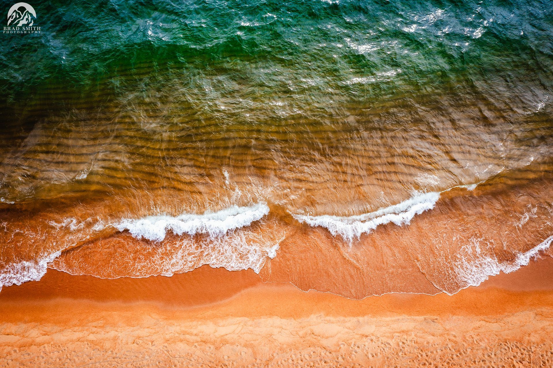 Aerial view of turquoise waves washing onto a golden sandy beach.