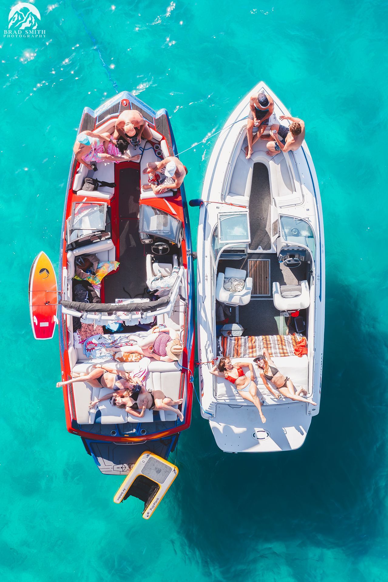 Two boats side by side on turquoise water with people relaxing aboard and a small float nearby