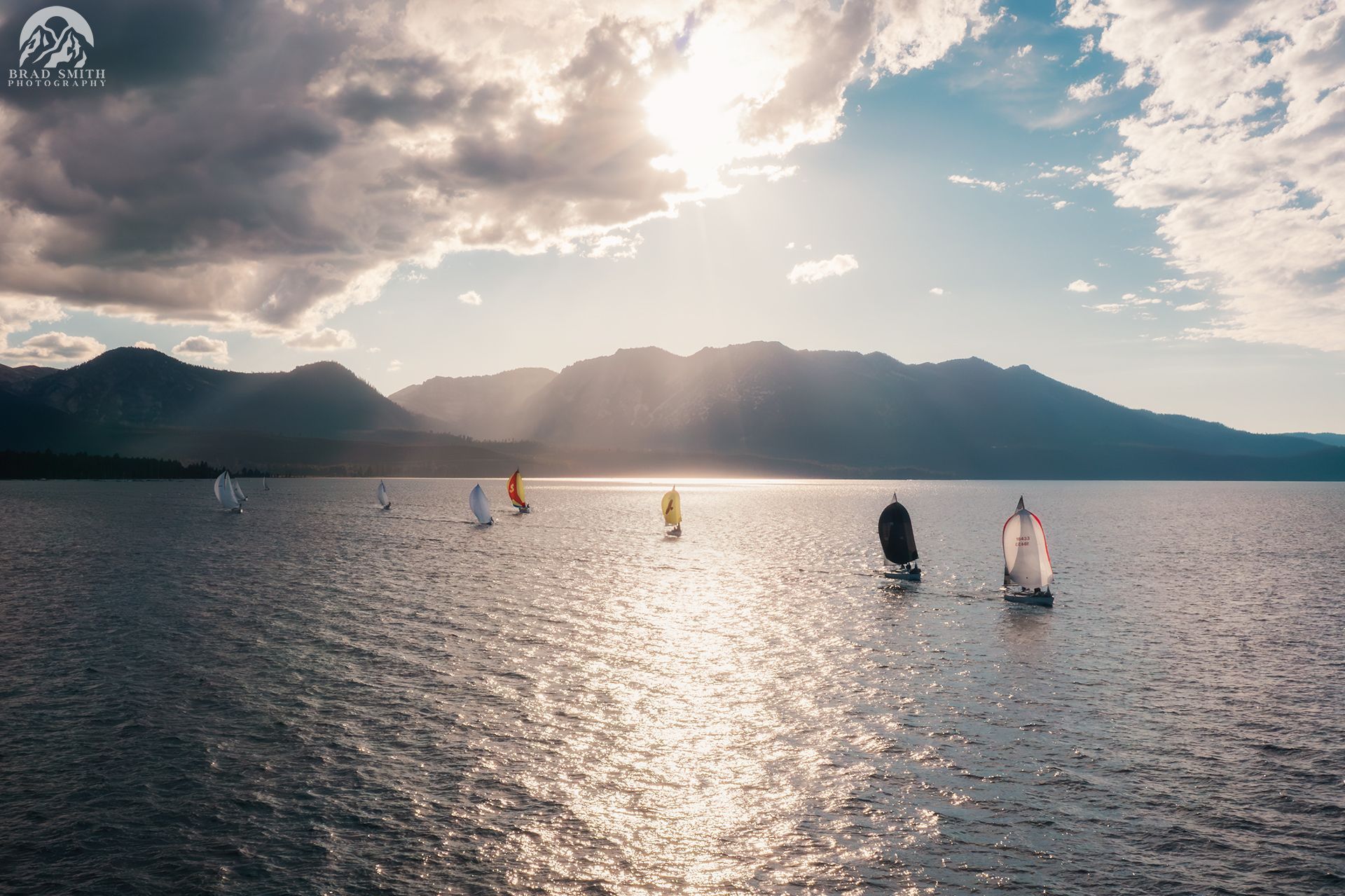 Sailboats on a sunlit lake with mountains and clouds in the background