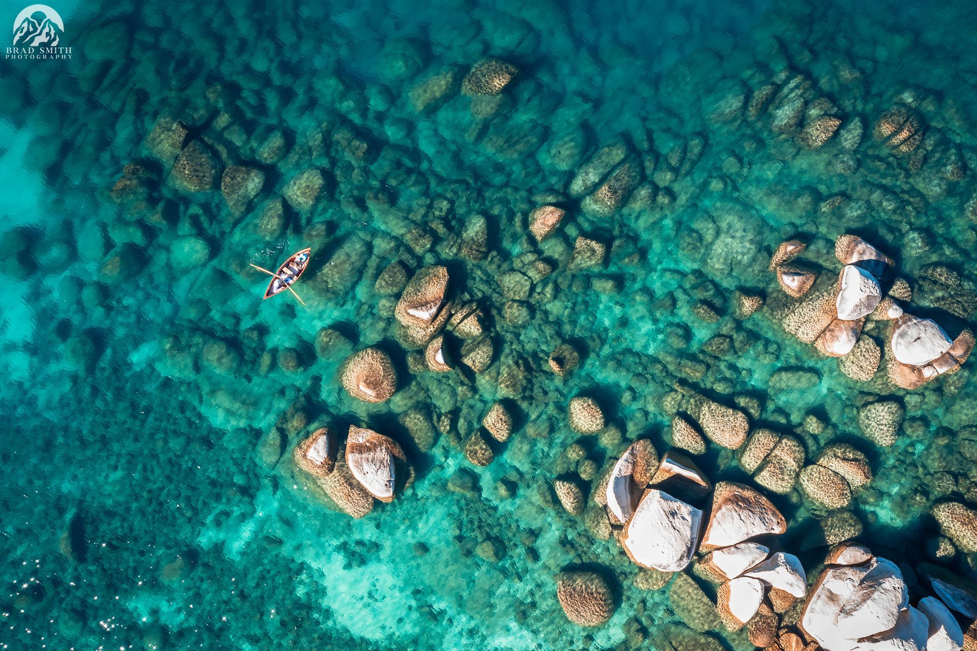 Aerial view of turquoise water with scattered rocks and a small boat near the left side.