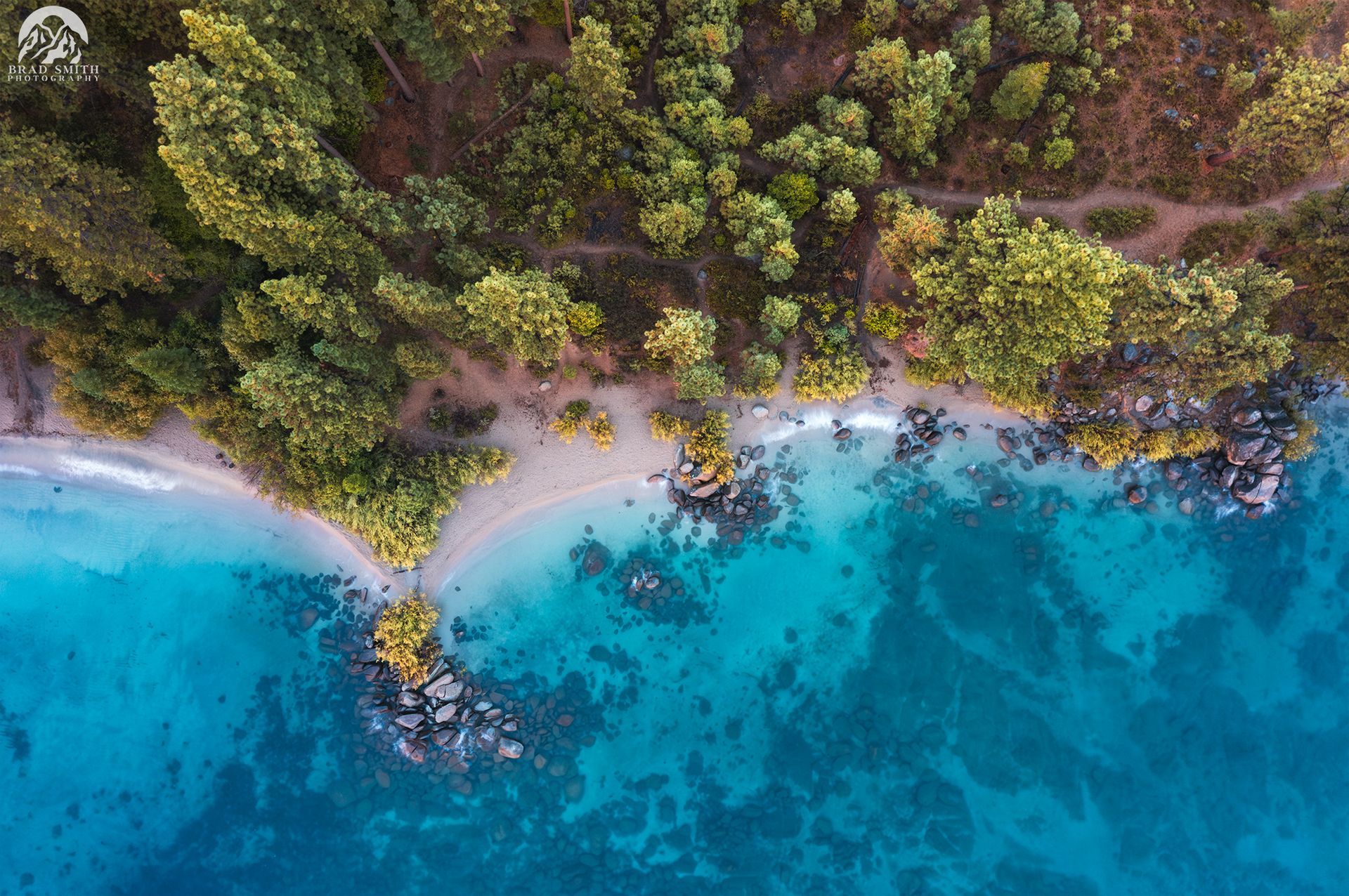Aerial view of a tropical beach with turquoise water, white sand, and dense green trees.
