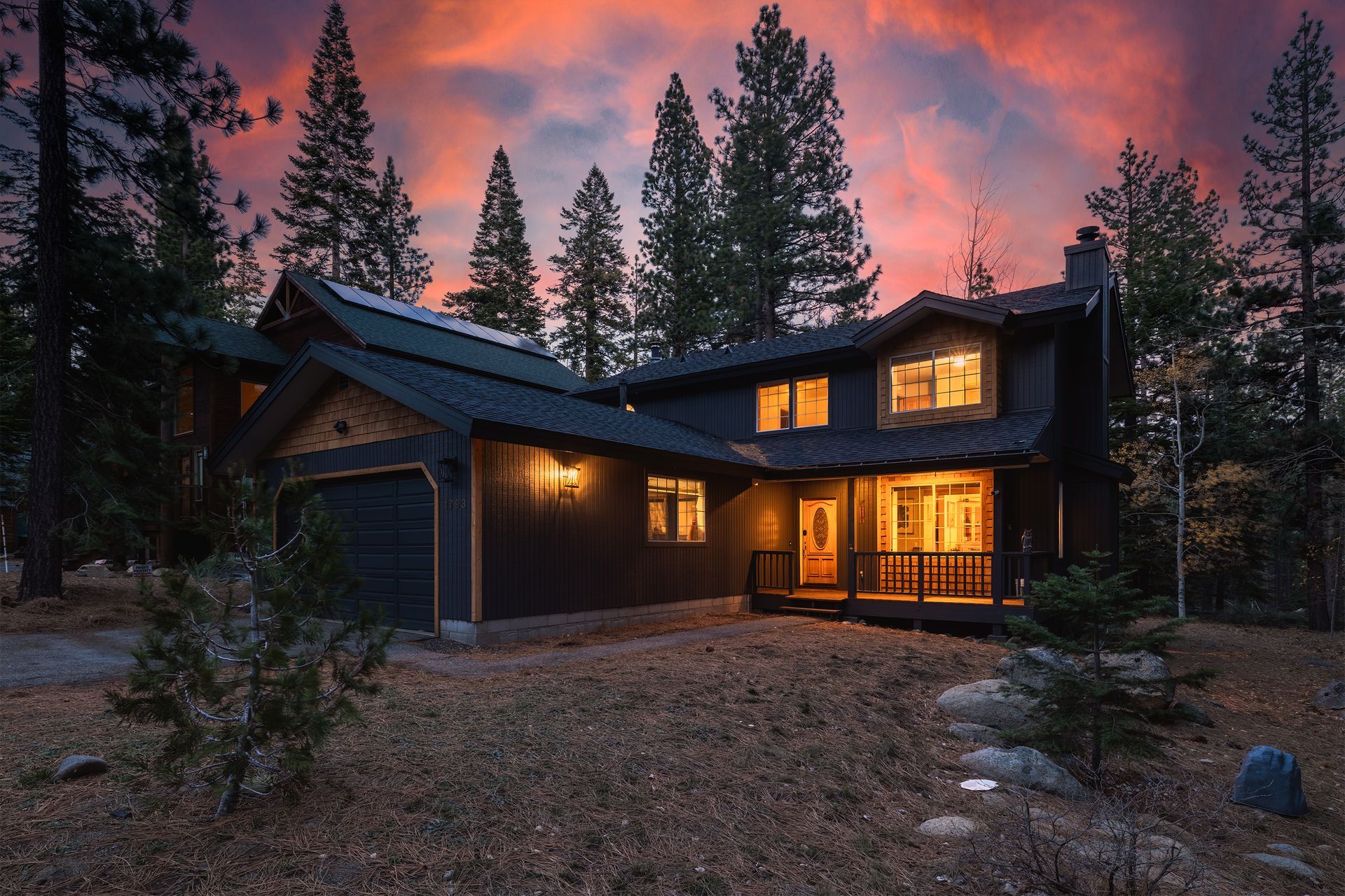A lit cabin at dusk in a forest, with warm windows glowing under a pink sky.