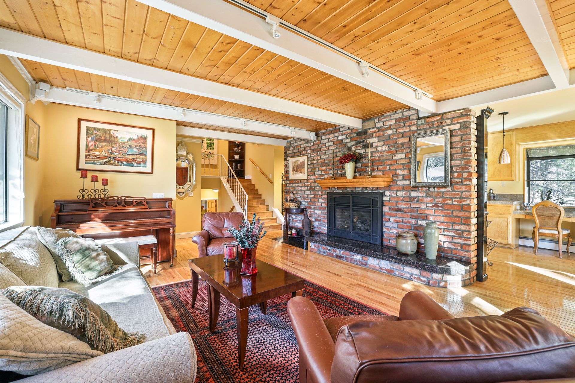 Cozy living room with stone fireplace, leather sofa, floral armchair, and wood-beamed ceiling