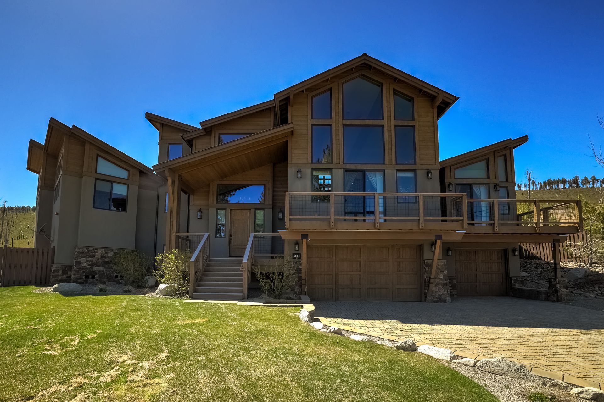 Modern brown house with large windows, front steps, and a grassy yard under a clear blue sky