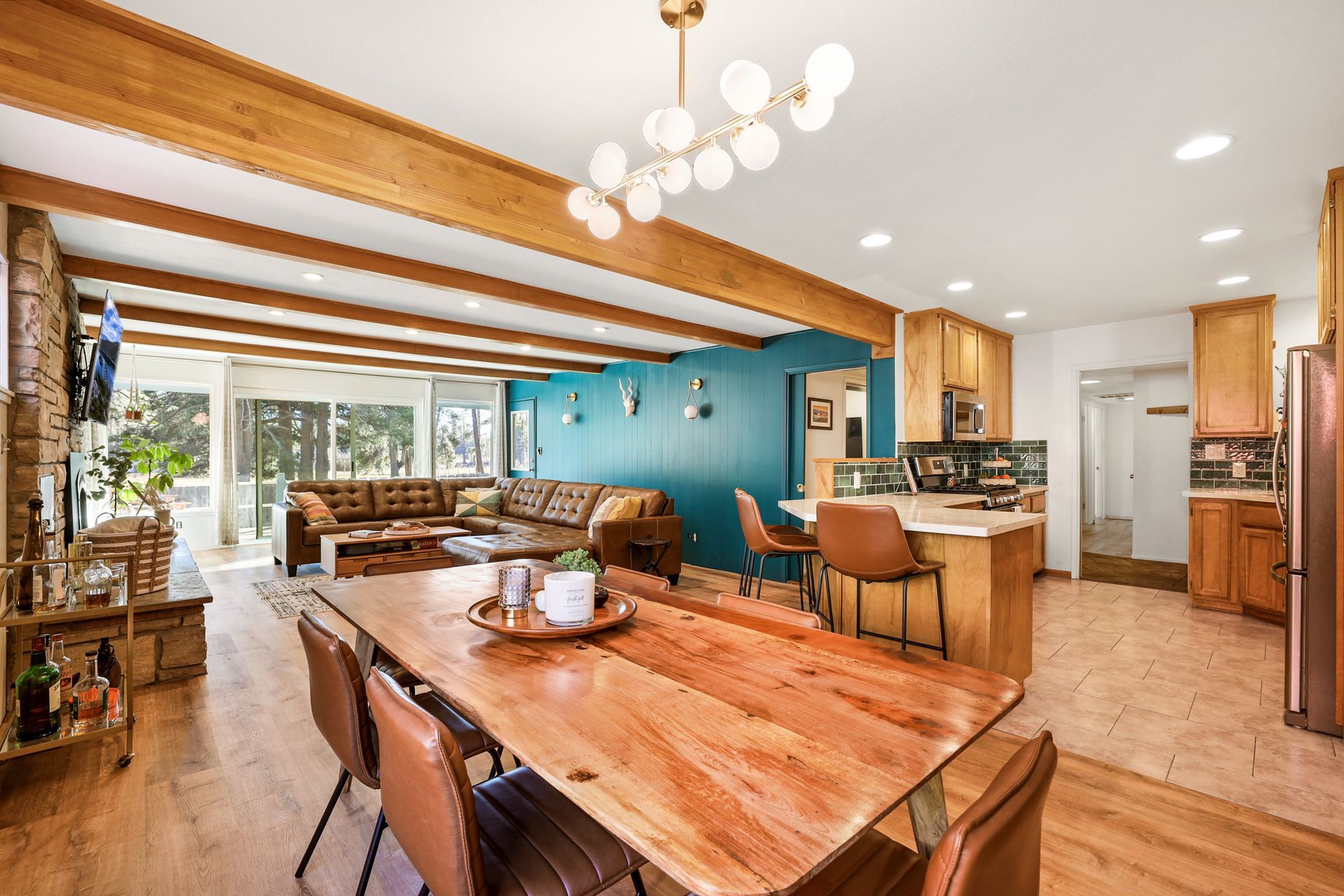 Open-plan kitchen and dining area with wood table, teal accent wall, and bar stools