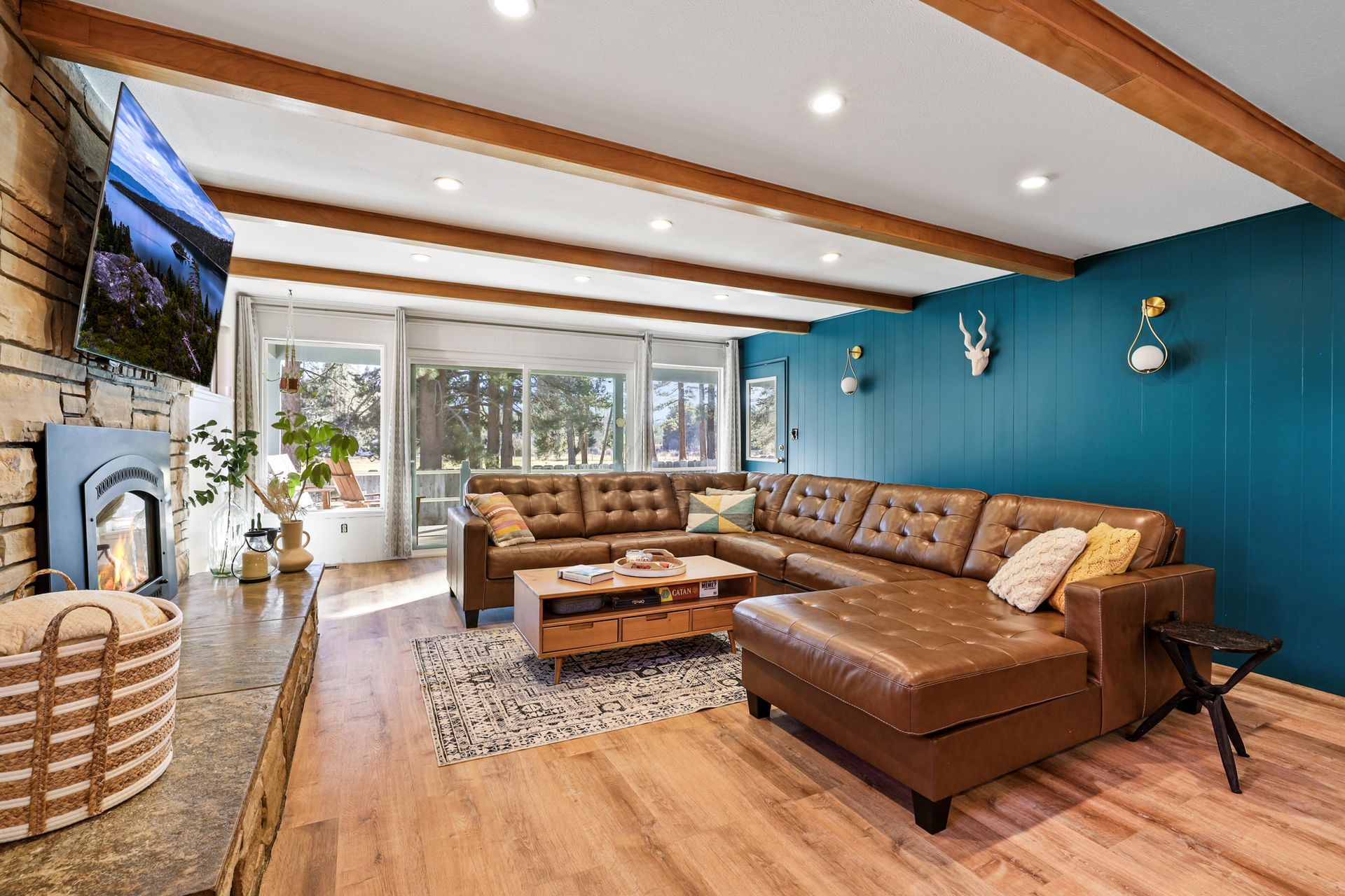 Bright living room with brown sectional sofa, teal accent wall, wooden beams, and large windows