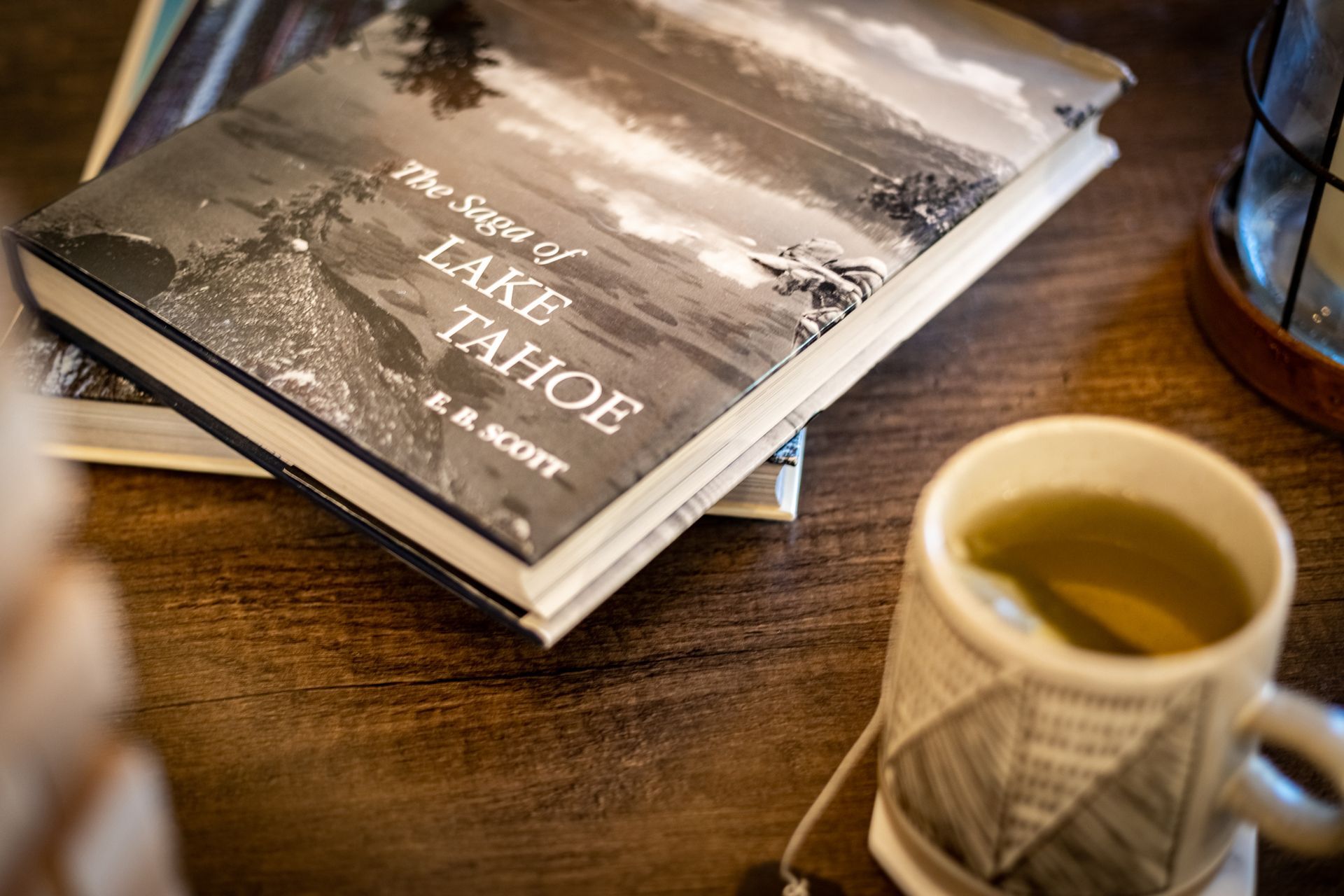 A stack of Lake Tahoe books beside a cup of tea on a wooden table.