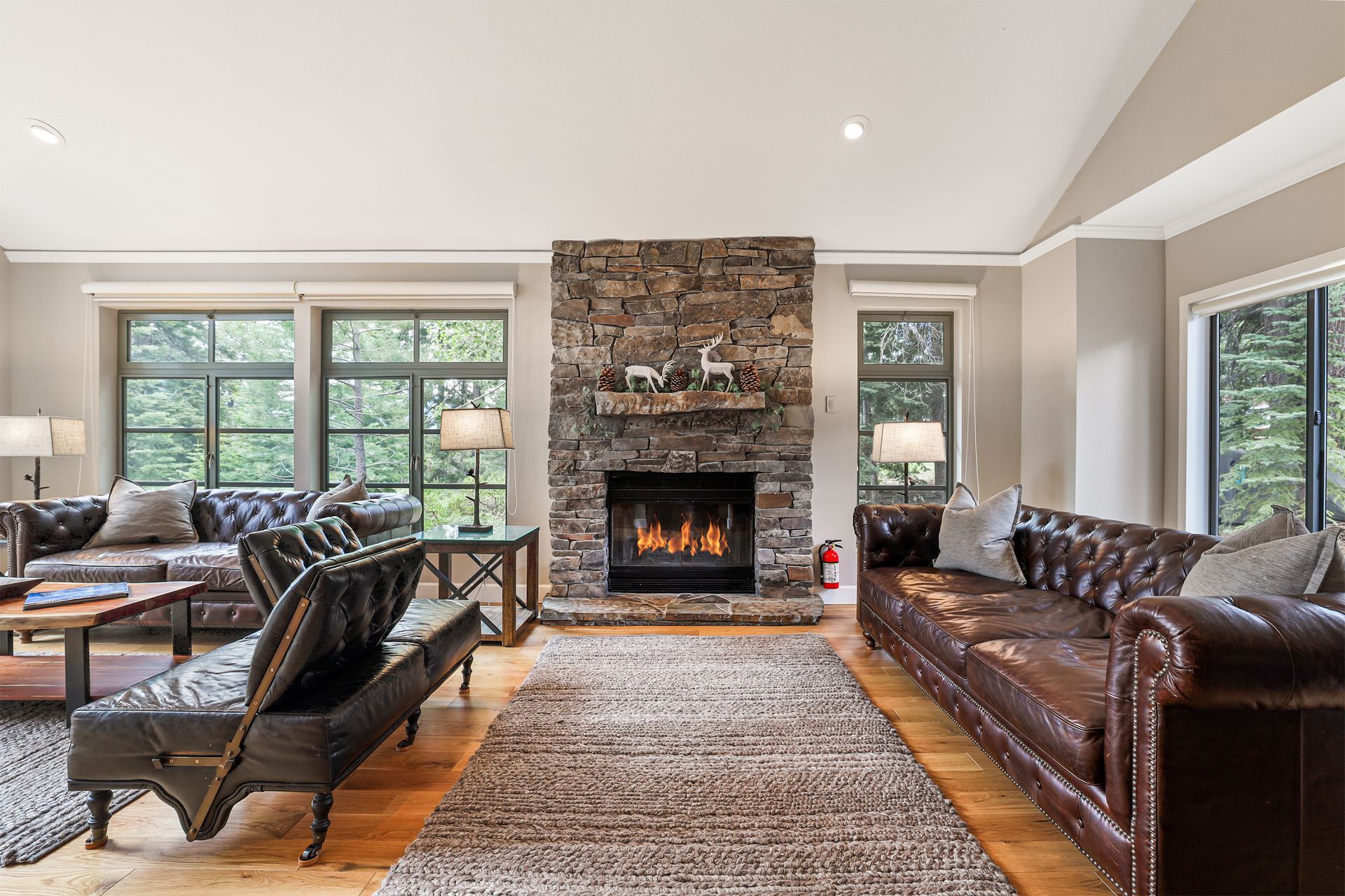 Elegant living room with stone fireplace, leather sofas, large windows, and hardwood floors