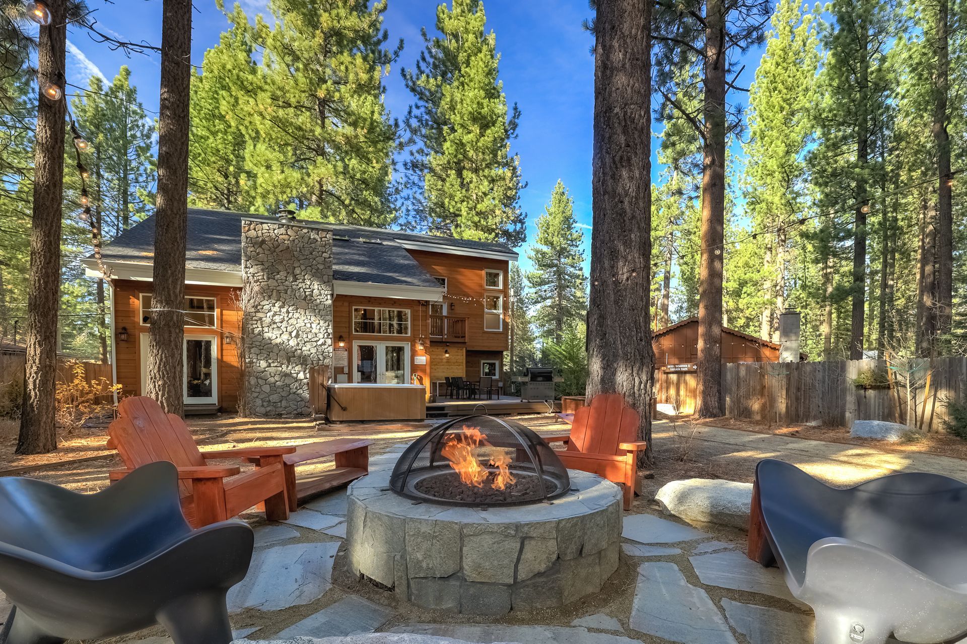 Outdoor fire pit seating area in front of a rustic cabin surrounded by tall pine trees