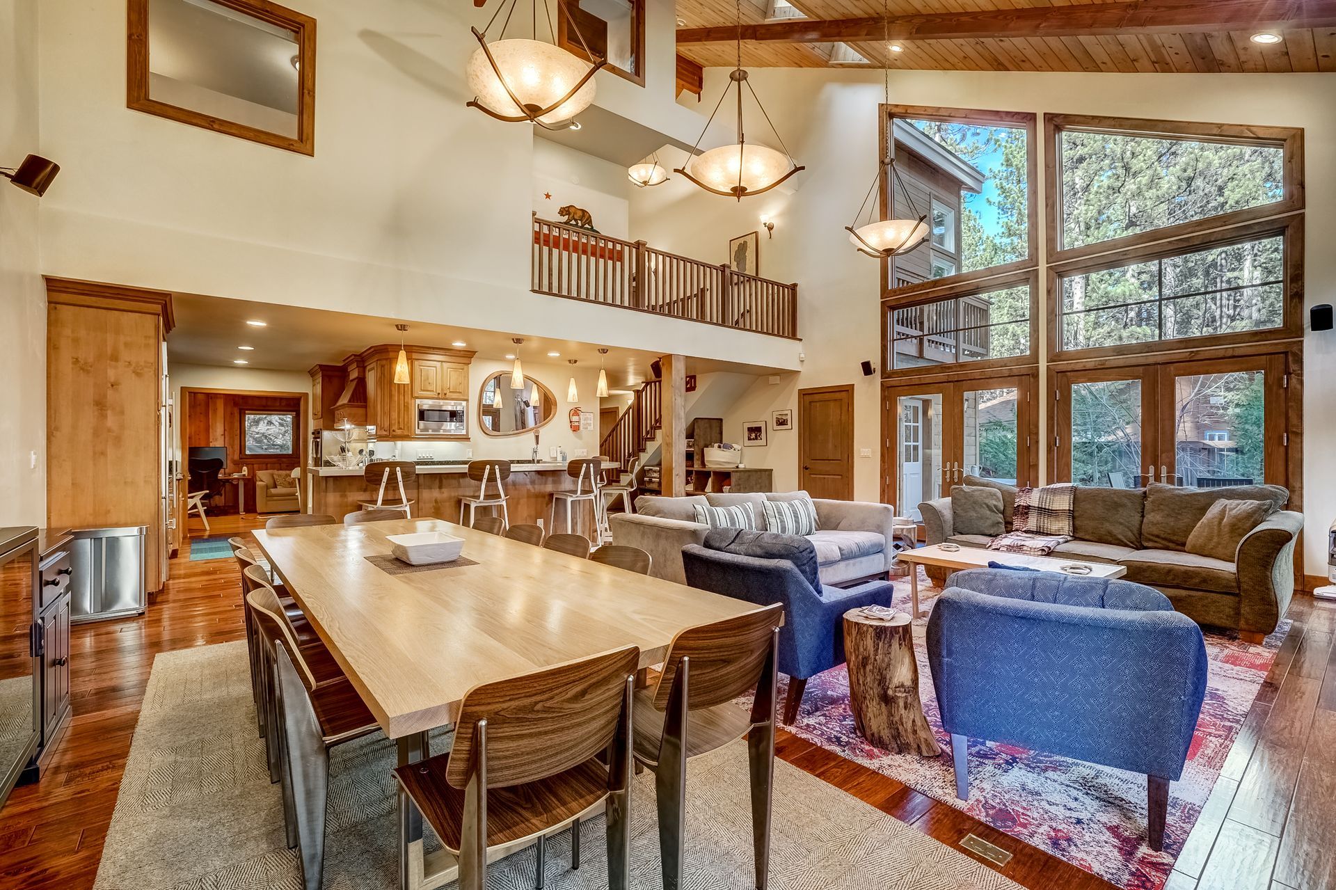 Bright modern living room with tall windows, wood beams, and blue chairs around a central table.