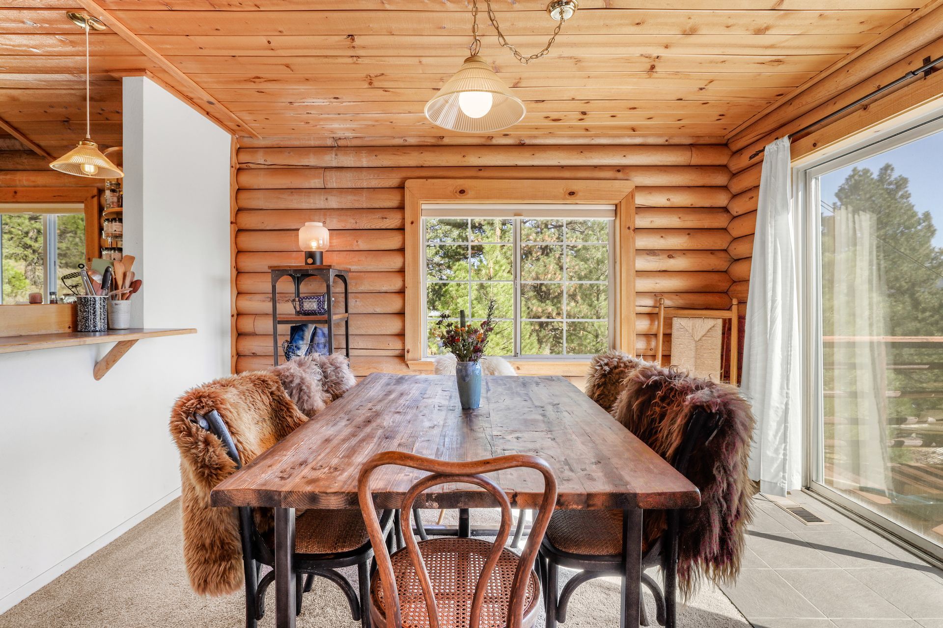 Cozy wooden dining room with rustic table, fur-covered chairs, and a large window overlooking trees