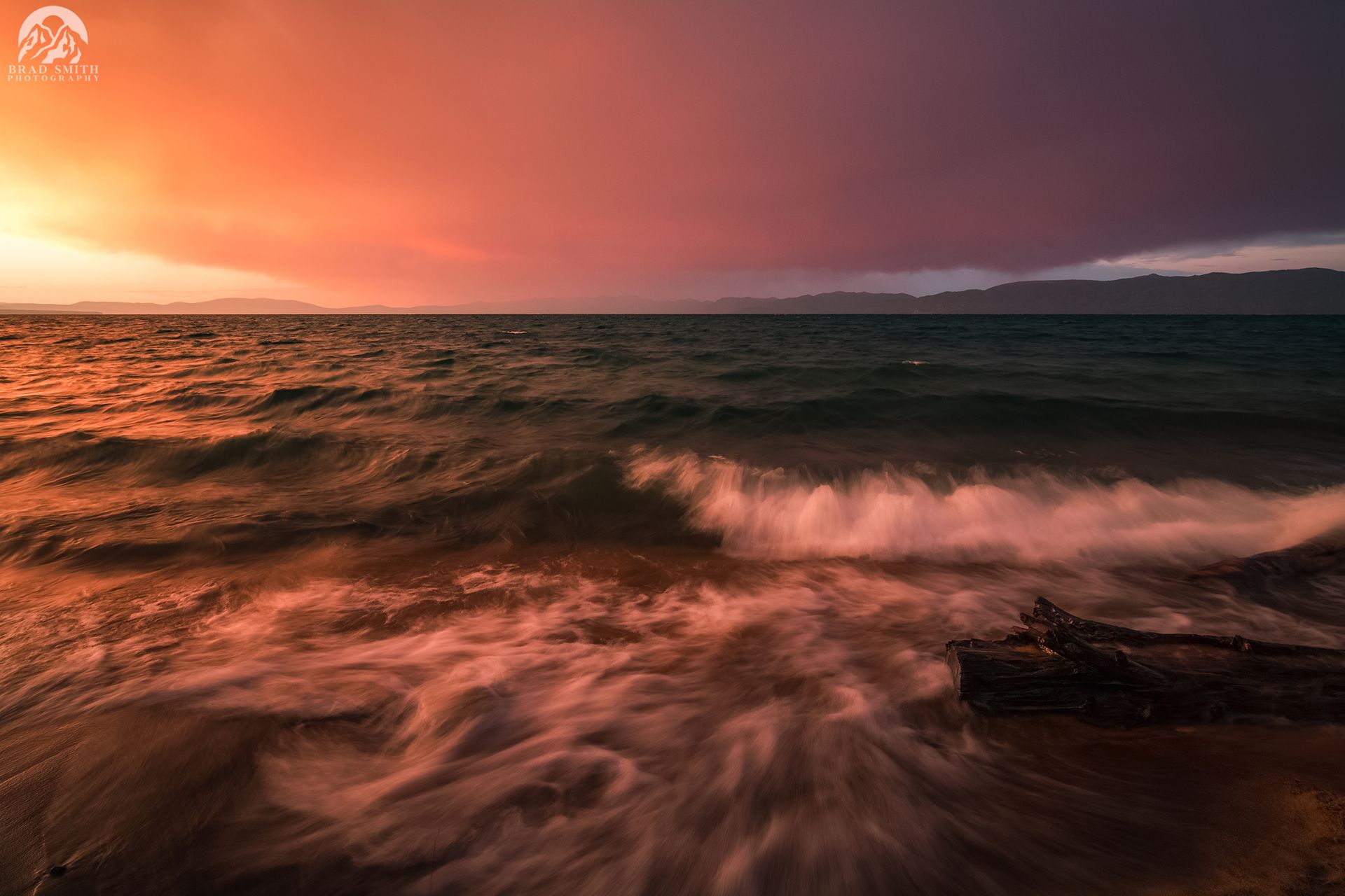 Sunset over a choppy ocean, with orange-pink sky and waves breaking on a rocky shore