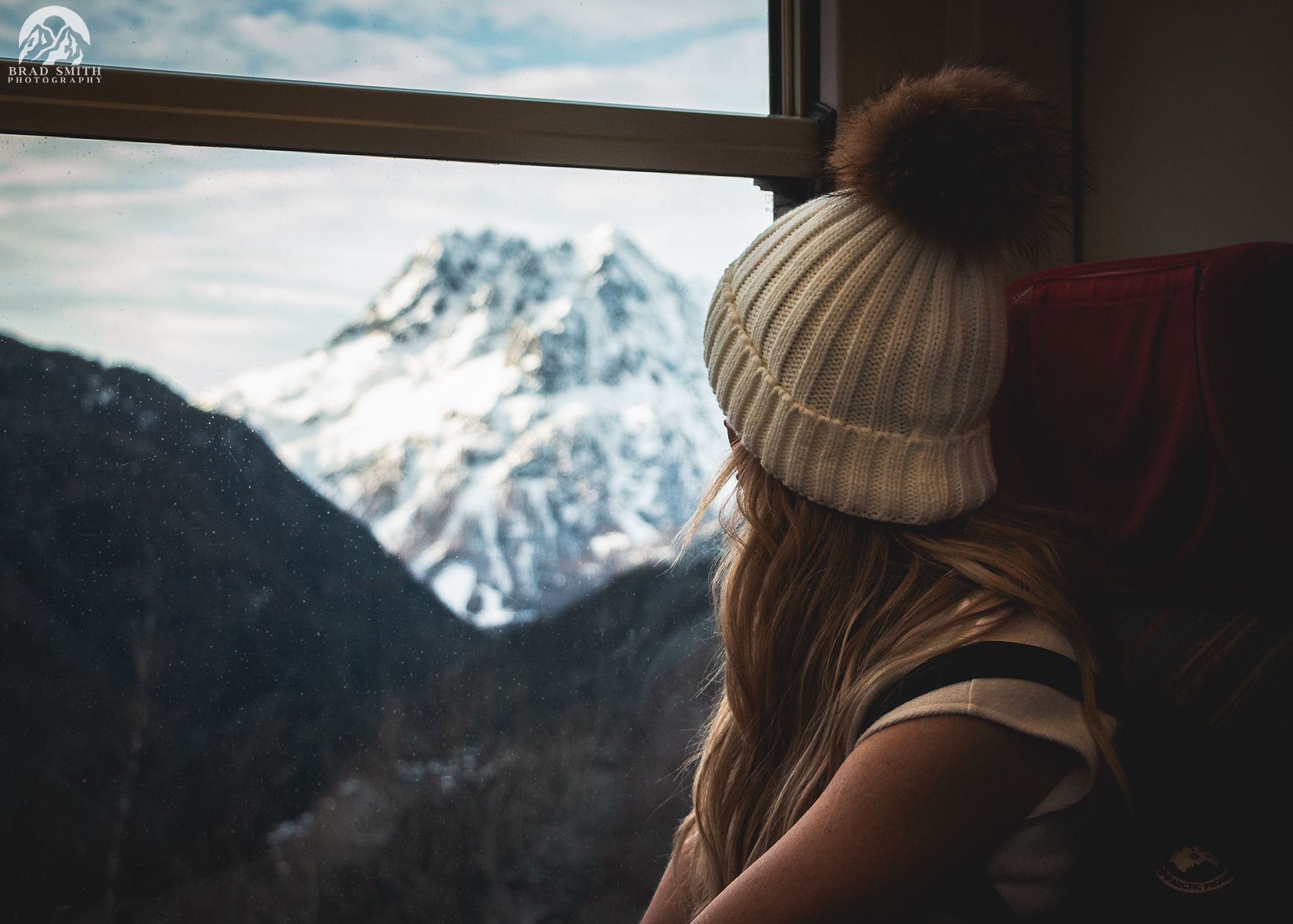 Woman in a knit hat gazing at snowy mountains from a train window