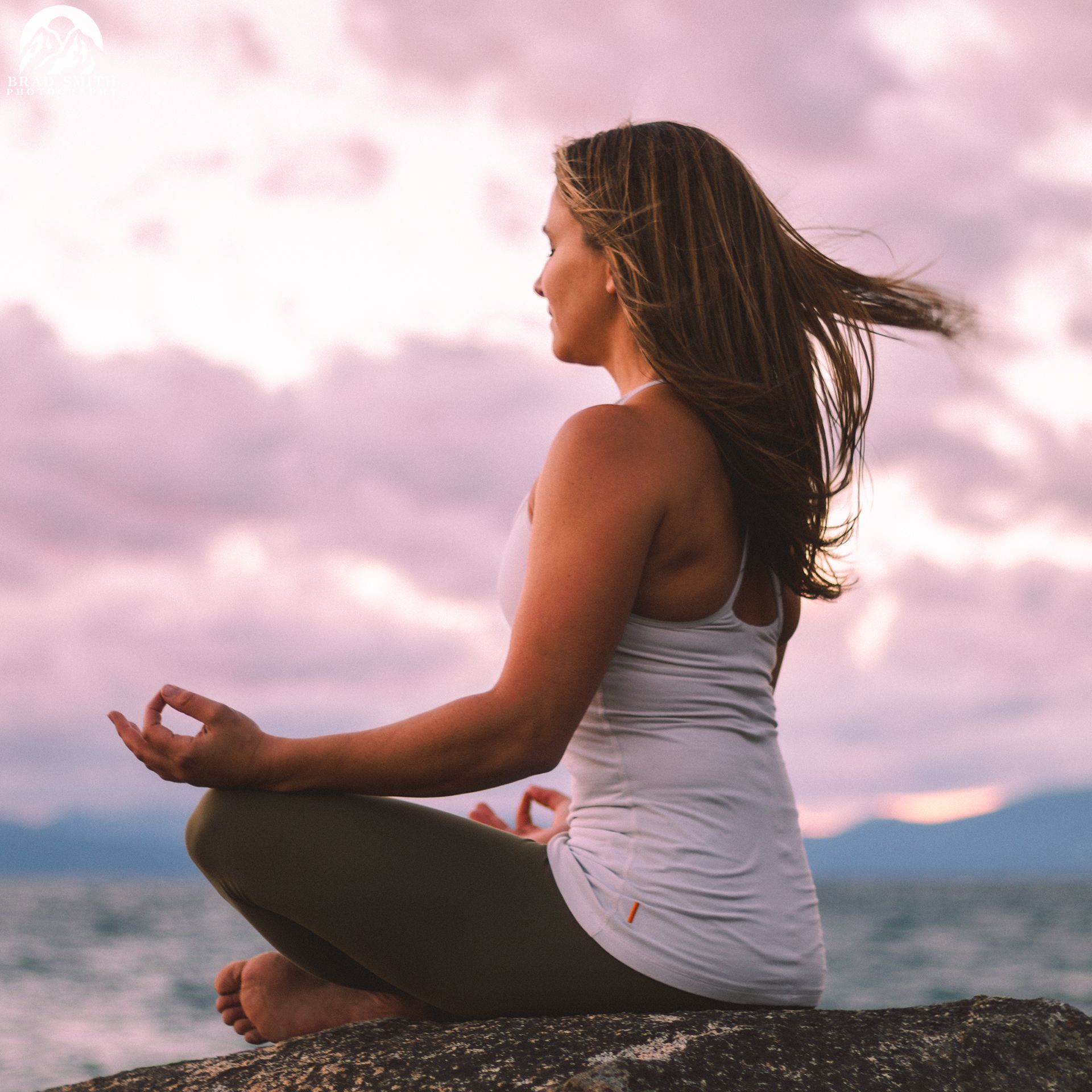 Person meditating on a rock by the sea at sunset, with pink clouds overhead.