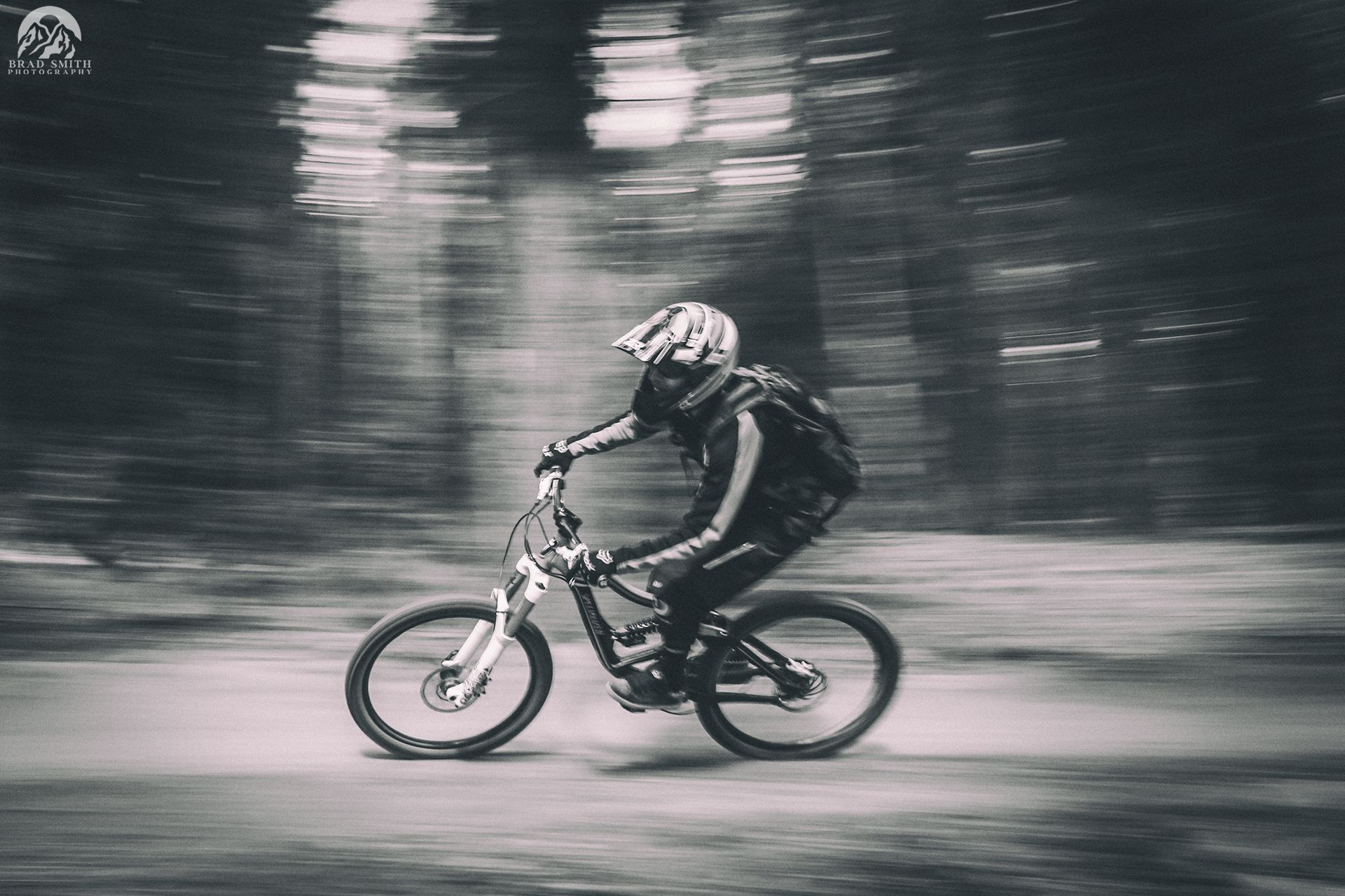 A cyclist rides a mountain bike through a blurred forest trail at speed.