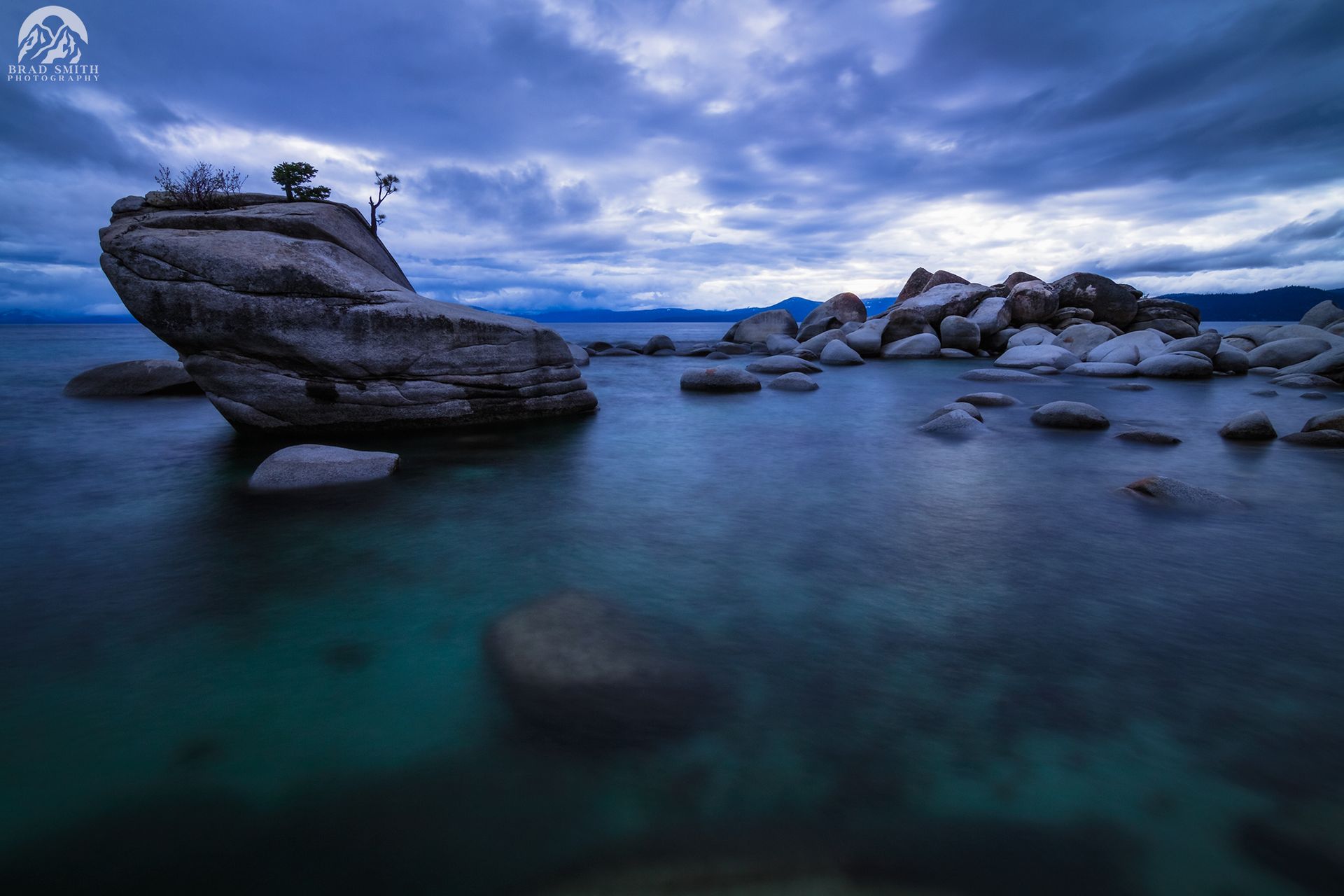 Blue twilight seascape with rocky outcrops and calm turquoise water under a cloudy sky