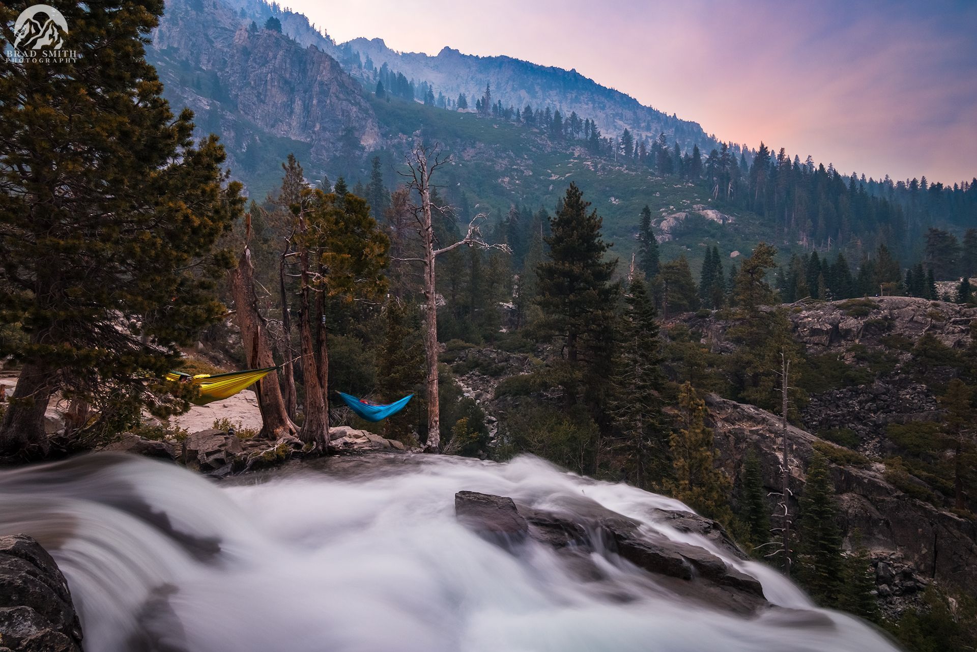 Mountain stream flowing past a blue hammock and tall pines at dusk