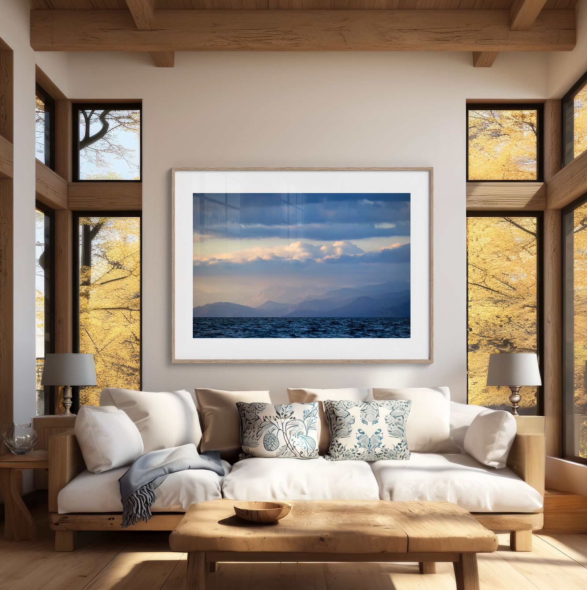 Cozy living room with white sofa, wooden coffee table, and framed landscape art by large windows.