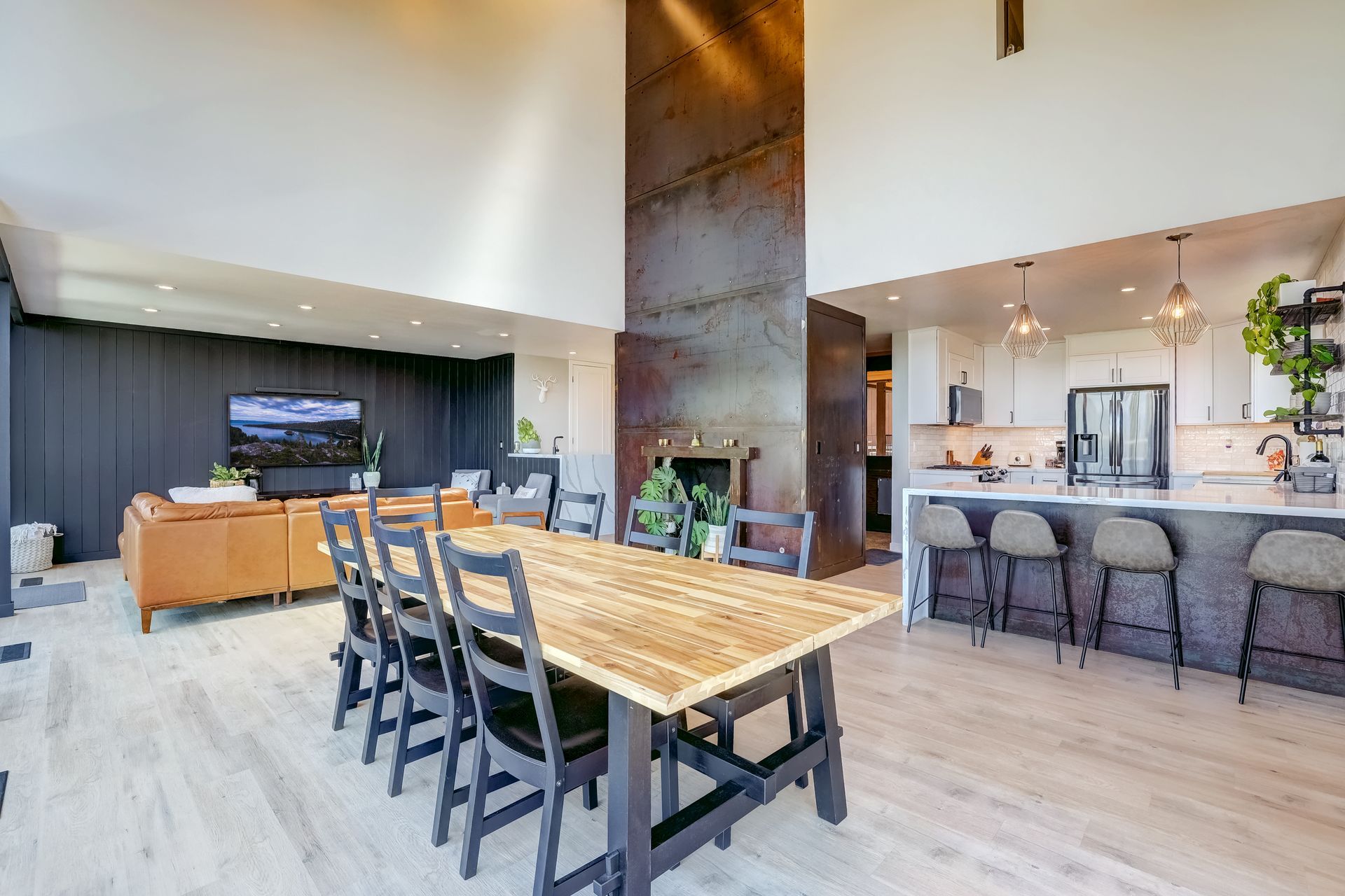 Modern open-concept living area with wood dining table, bar stools, and a kitchen island with pendant lights.