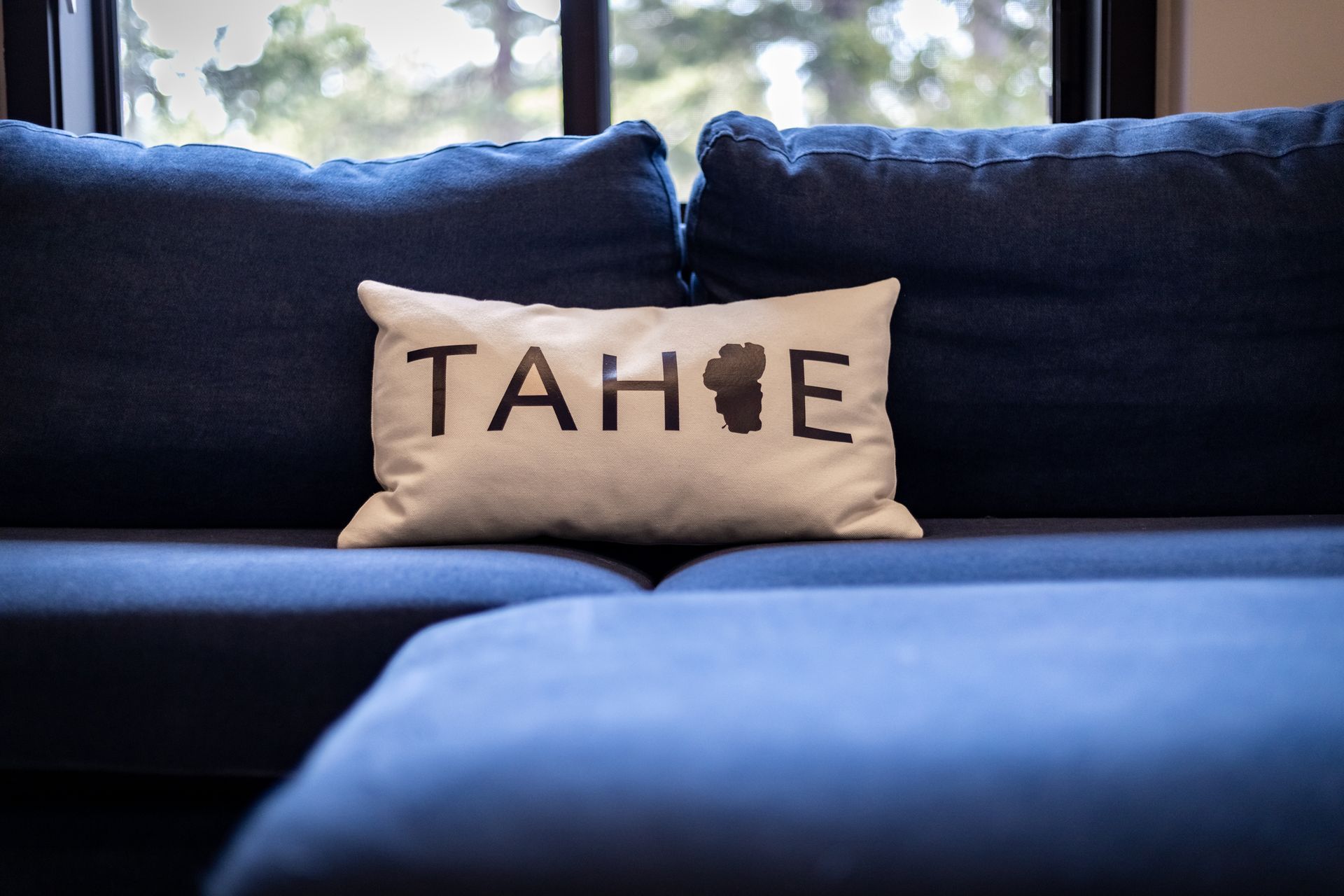 Blue couch with a beige pillow embroidered “TAHOE” in the center.