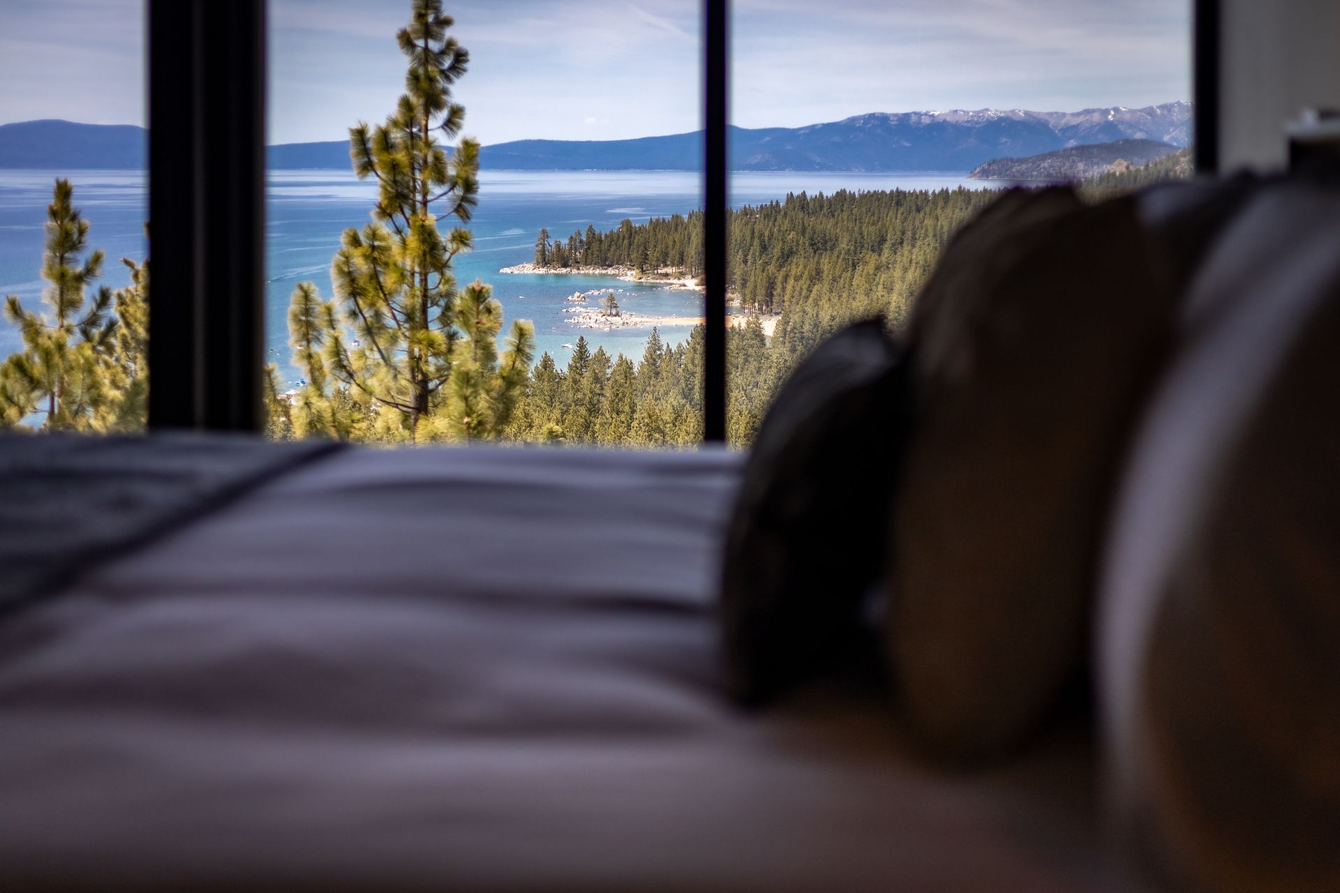 Lake view through bedroom windows with a bed in the foreground