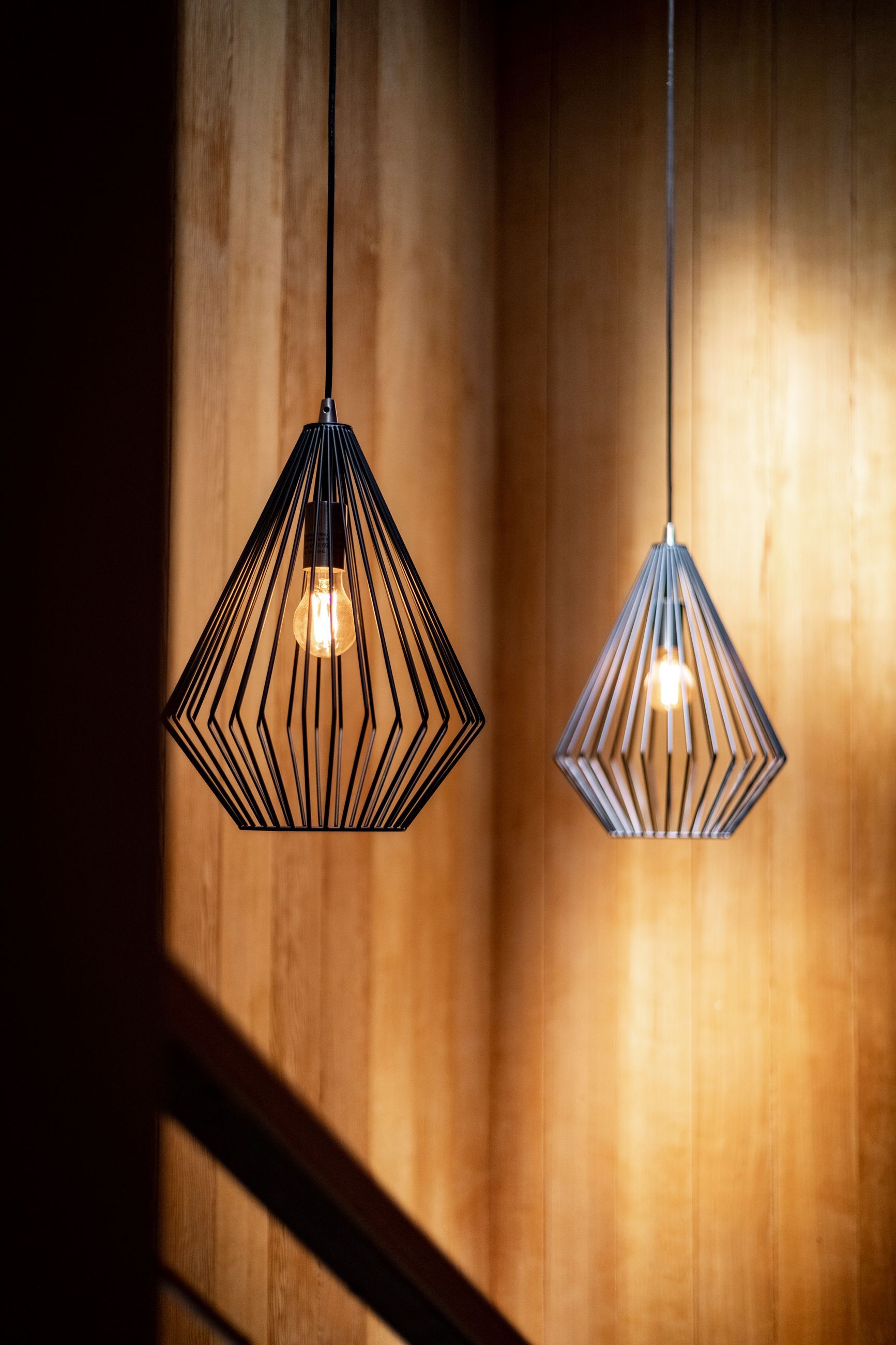 Two geometric pendant lights glowing against a warm wooden wall, casting soft shadows.