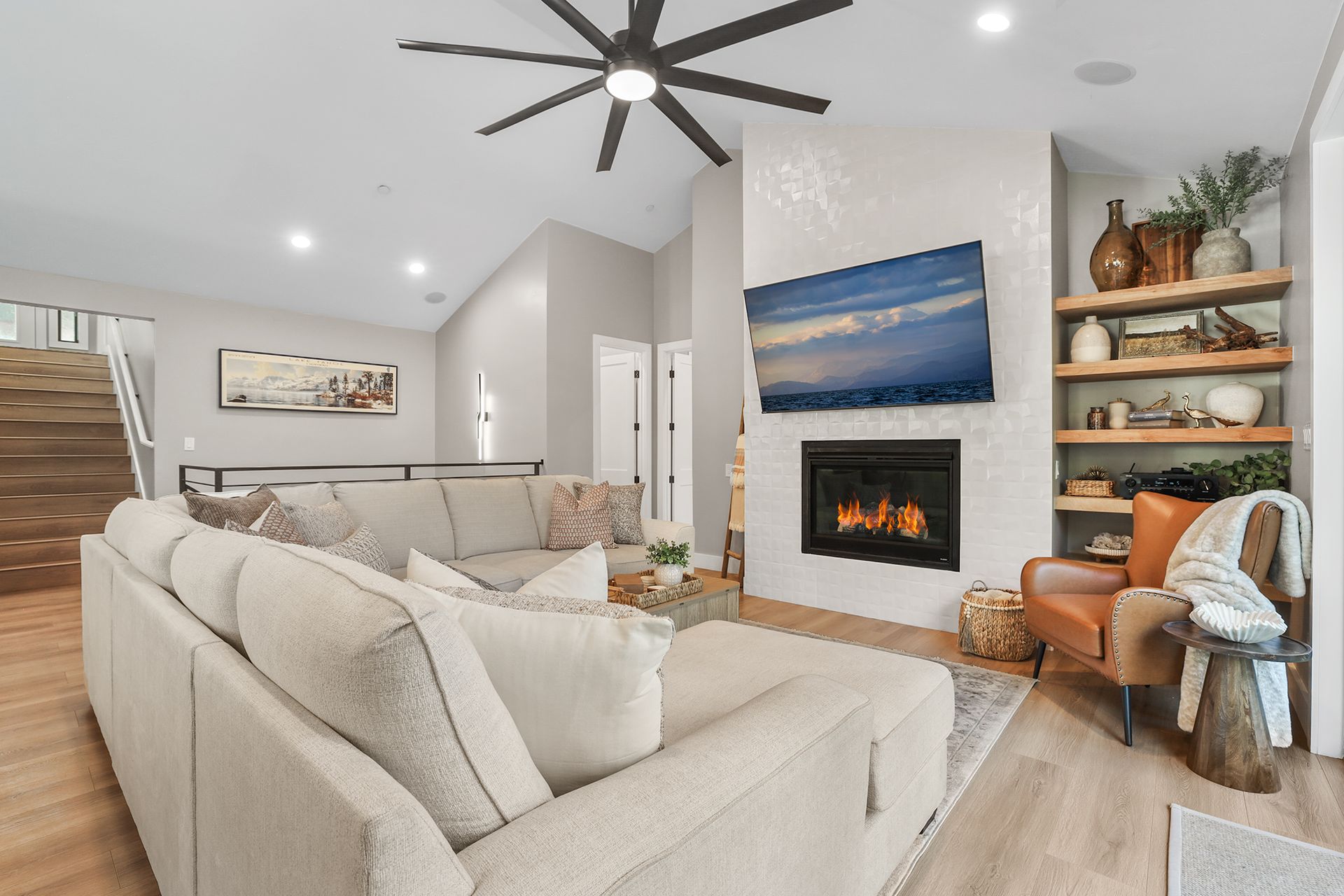 Bright living room with beige sofas, fireplace, large fan, and wall art under recessed lighting