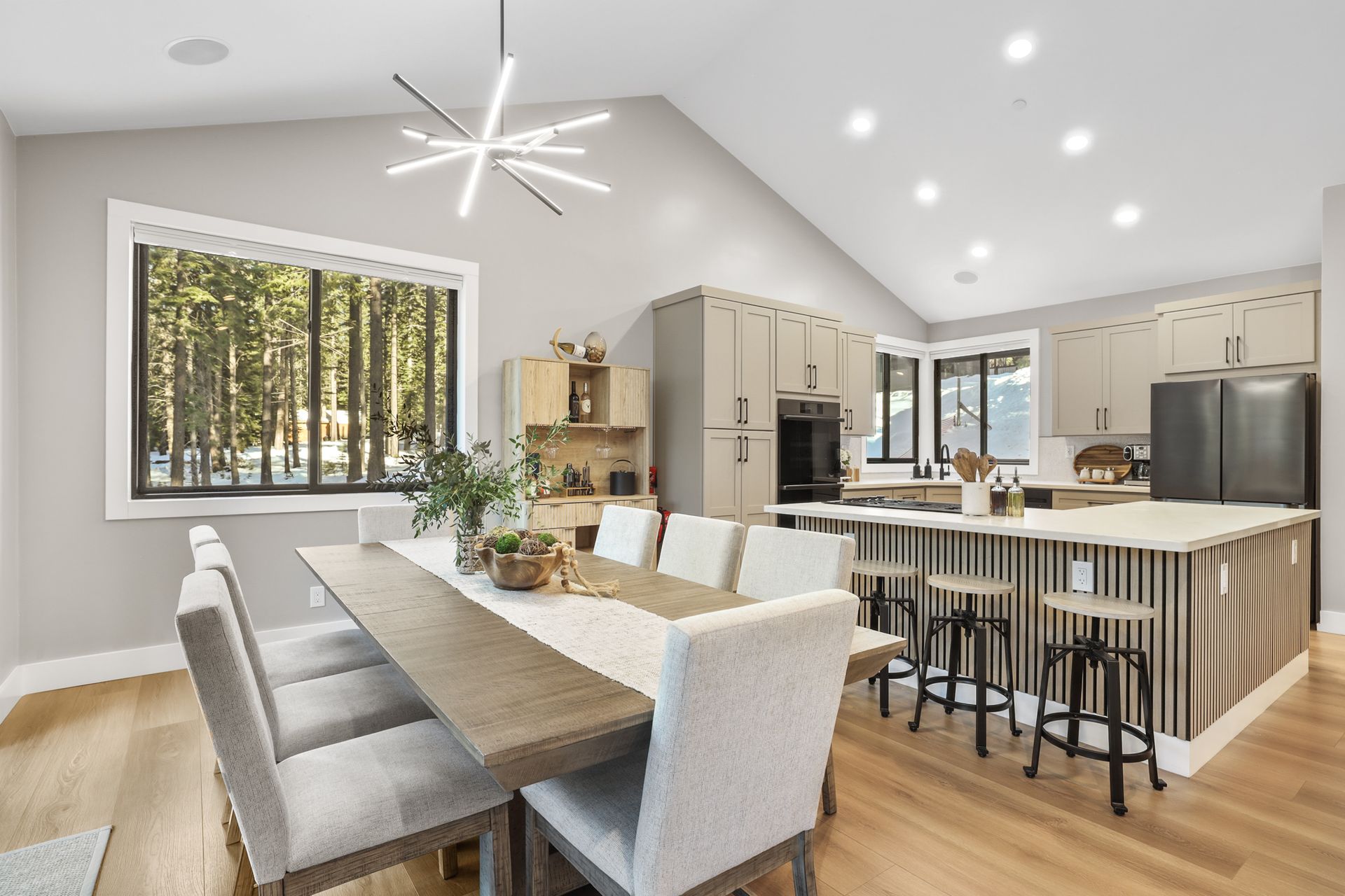 Bright open-plan kitchen and dining room with wood floors, white cabinets, island seating, and large windows